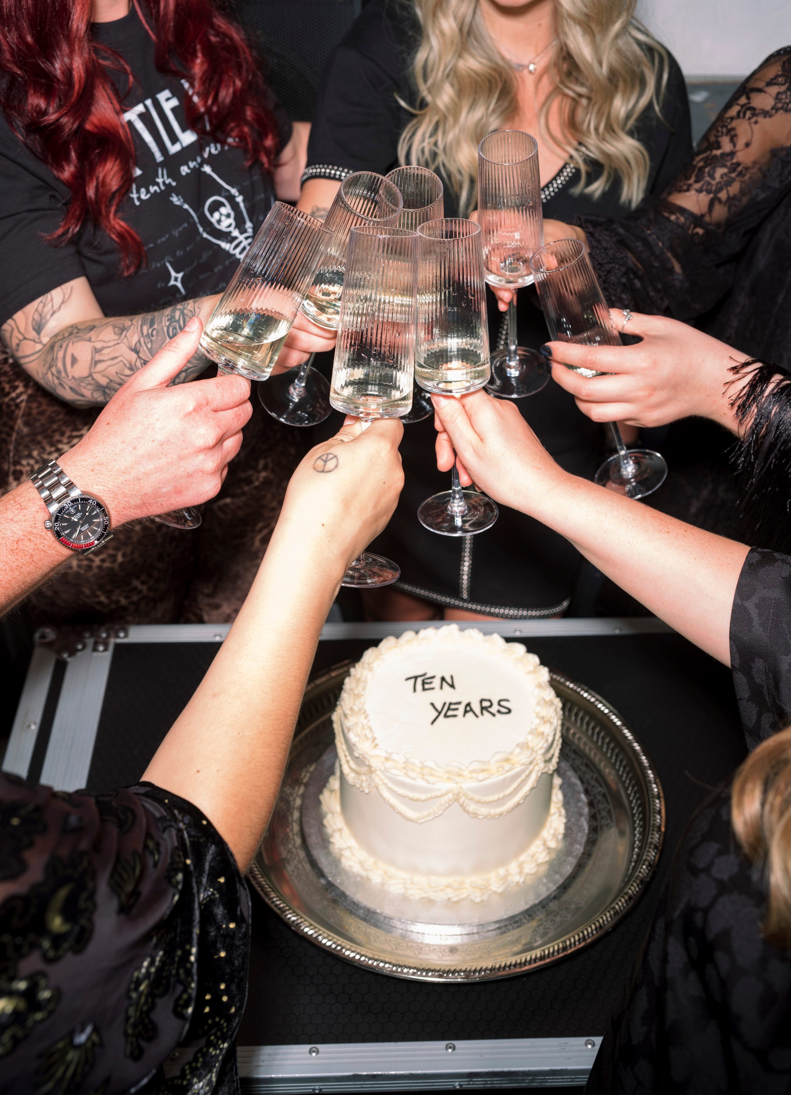 Little Lies Team toasting with champagne glasses around a cake celebrating 'Ten Years' on aflight case