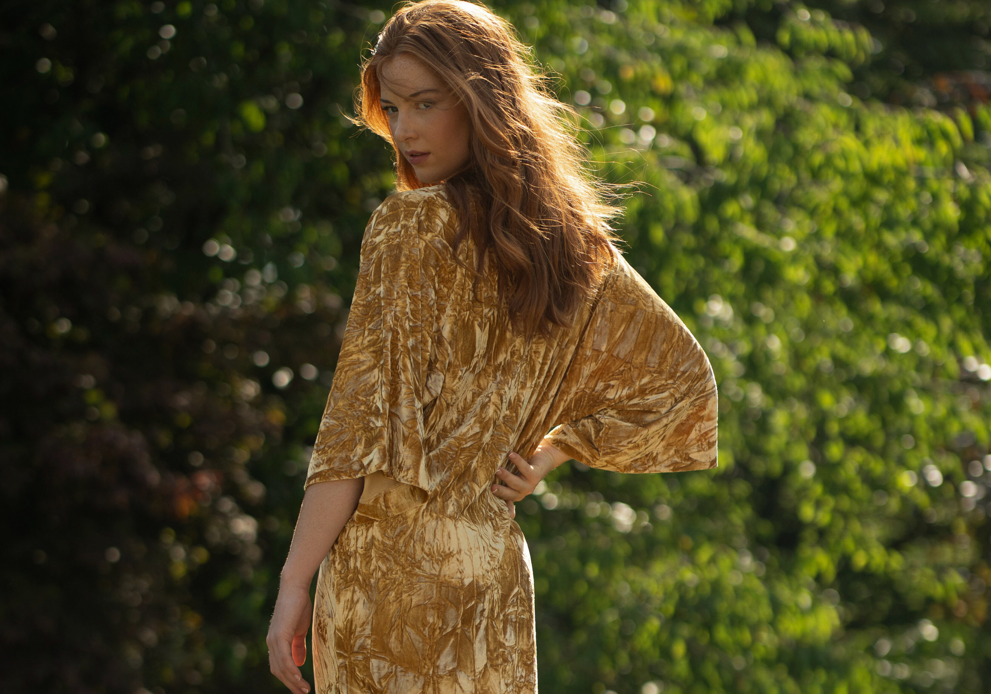 Anna in Rumours Ochre crushed Velvet Midi dress standing in the country estate gardens at the Byre at Inchyra.