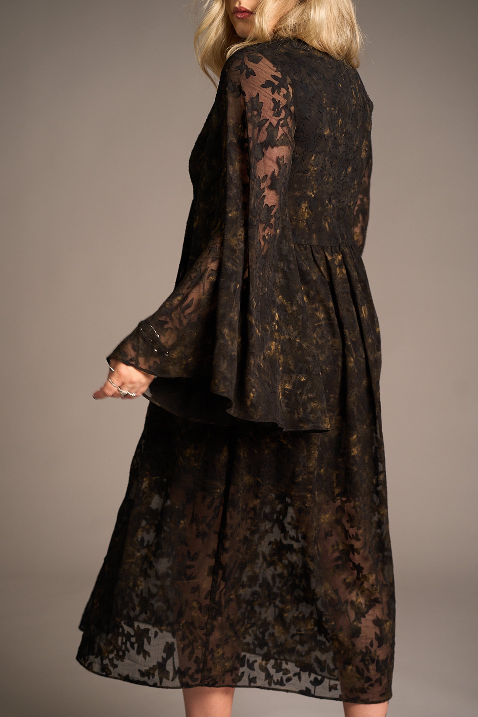 Side view of Erin wearing the Bella Donna Midi Dress in sheer black fabric with intricate floral patterns and flared sleeves, Stevie Nicks inspired styling studio