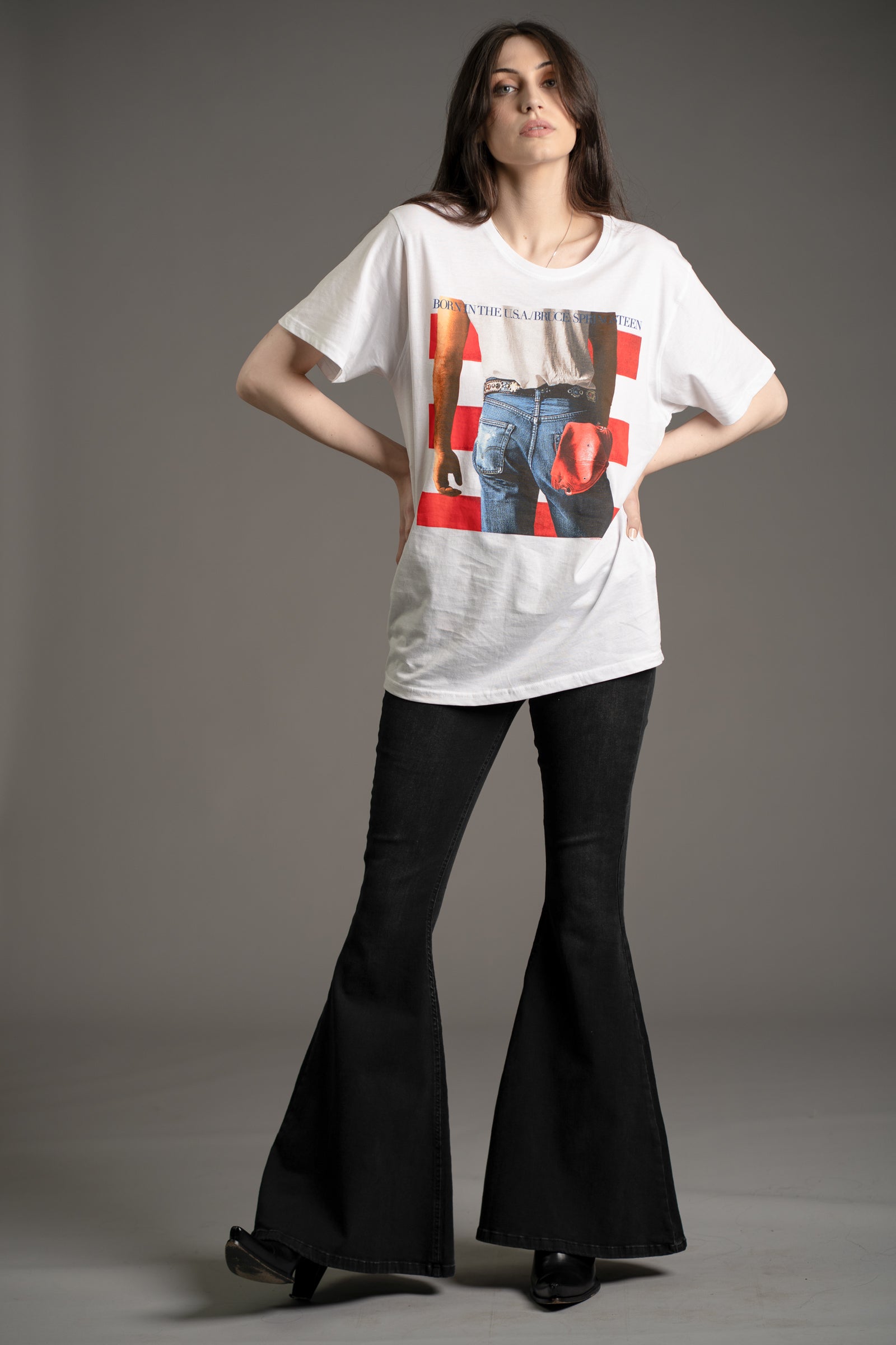 Model Andie wears white Bruce Springsteen Born in the USA graphic tee styled with Little Lies Hendrix Denim flares and heeled boots
