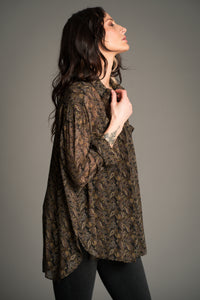 Victoria wears the Cinnamon Girl Paisley Chiffon Shirt in an oversized silhouette, shown side-on to display the flowing lightweight fabric and all‑over boho paisley print.
