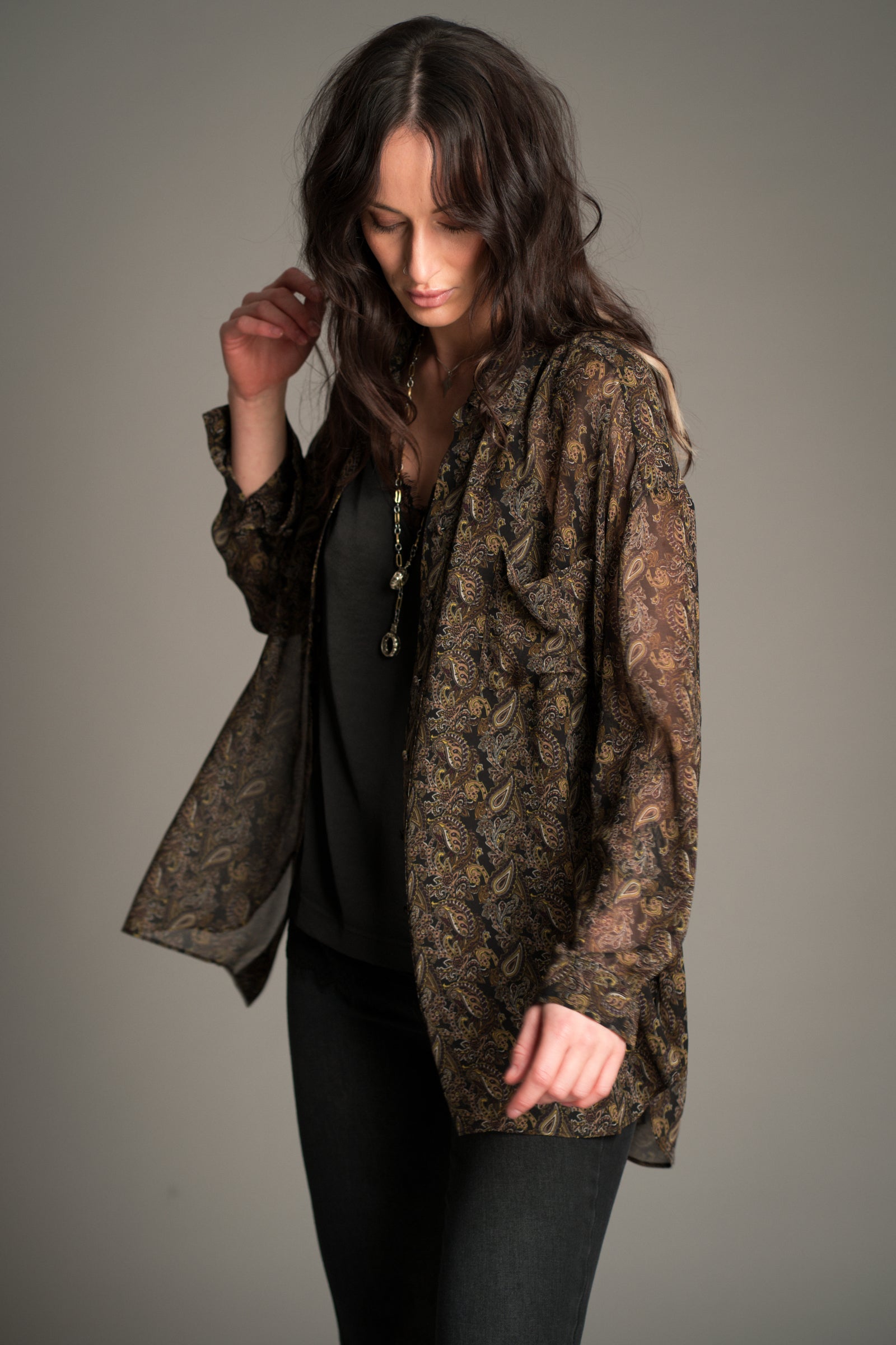 Victoria wears the Cinnamon Girl Paisley Chiffon Shirt styled open over a satin cami, showing the lightweight sheer fabric and all‑over boho paisley print.