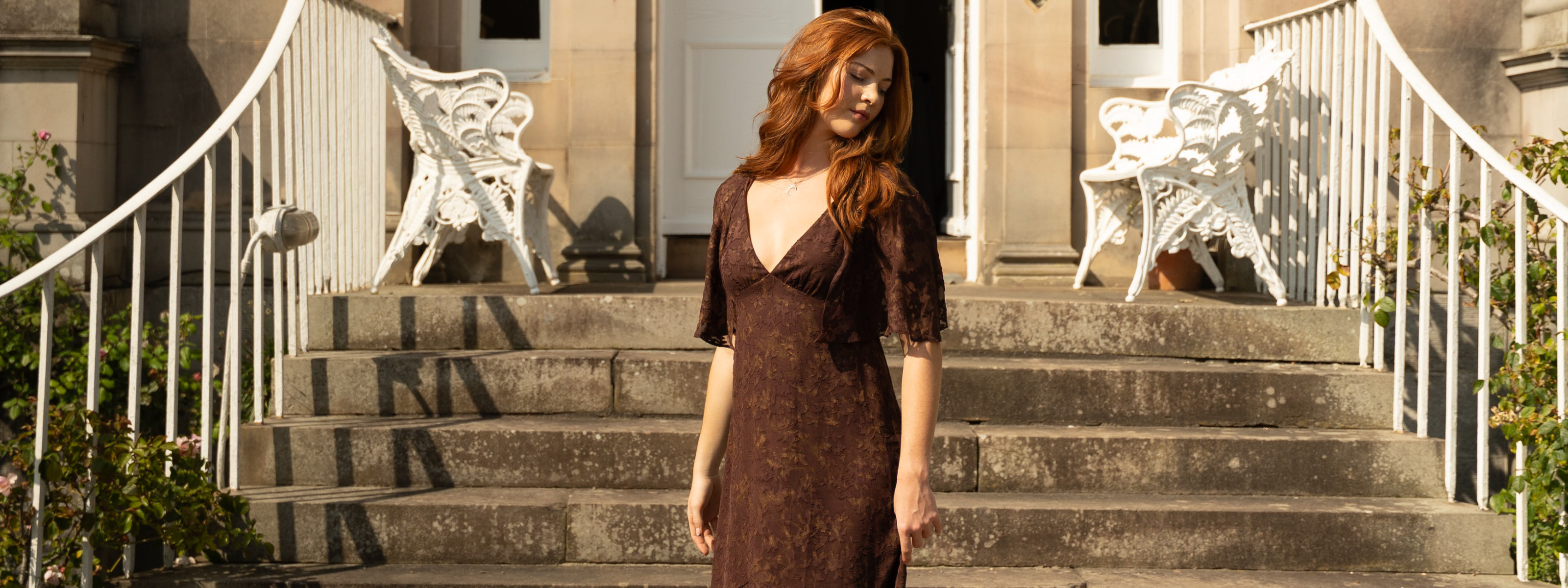 Anna in Brown Sugar Chiffon Midi Dress, styled with Sterling Silver Crescent Moon Pendant in front of a staircase outside.
