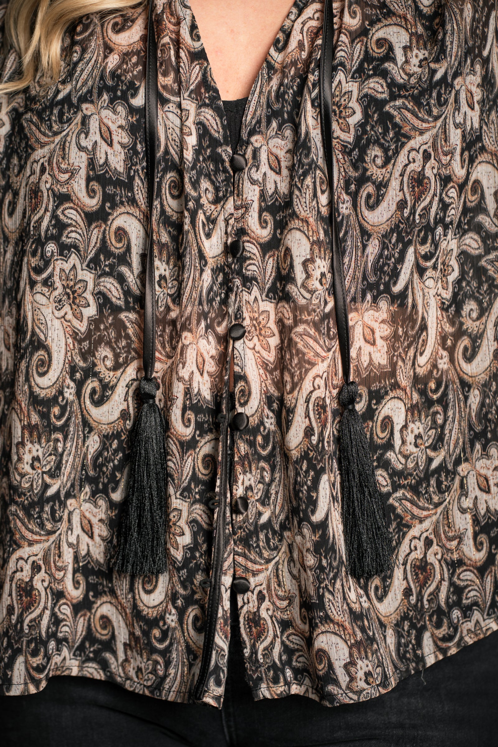 Close-up of Little Lies Eleanor smock top showing tassel tie neckline, button detailing and sheer paisley fabric in neutral tones
