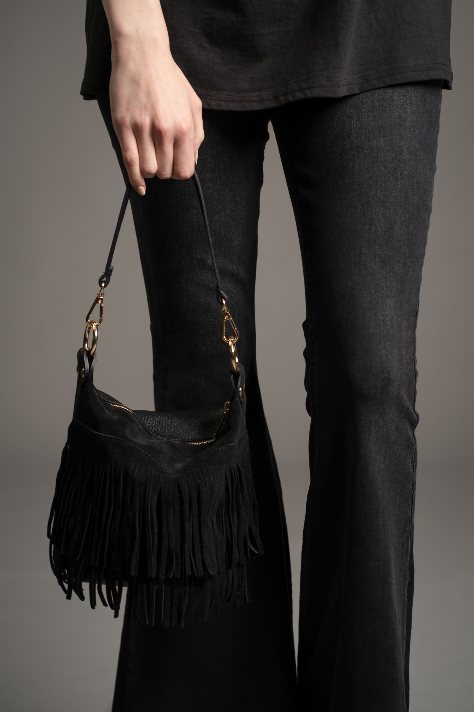 Model holding Gemini Genuine Leather Fringed Bucket Bag in black with gold hardware and layered fringe detail by Little Lies in studio setting