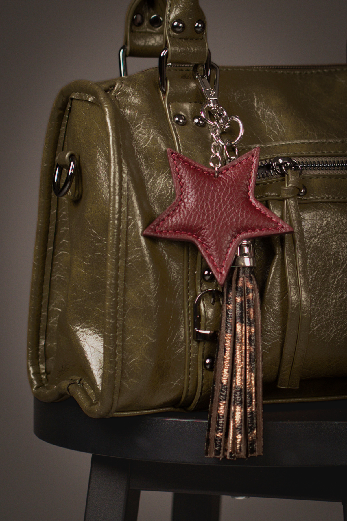 Little Lies burgundy leather star bag charm styled on an olive handbag with metallic tassel accessory and vintage-inspired hardware