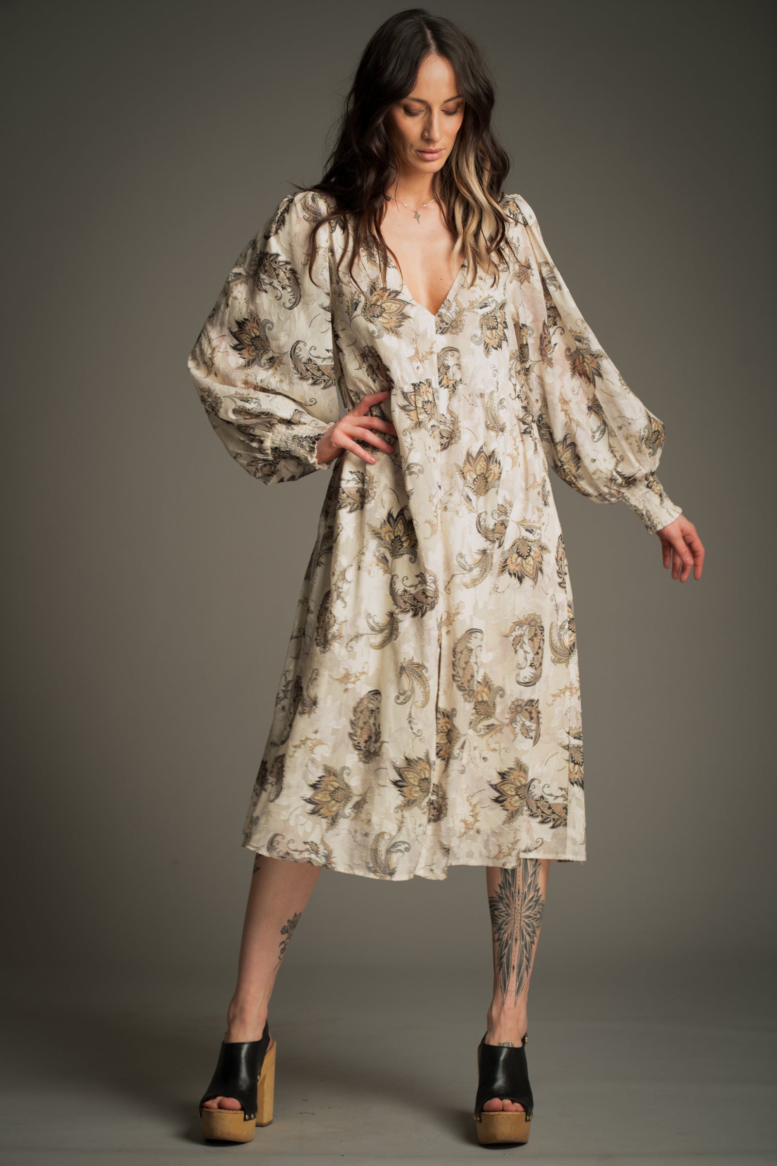 Victoria wears Little Lies Harvest Moon Paisley Midi Dress in cream with an intricate paisley print, full‑length view featuring voluminous long sleeves and a flowing midi silhouette, styled with platform sandals.