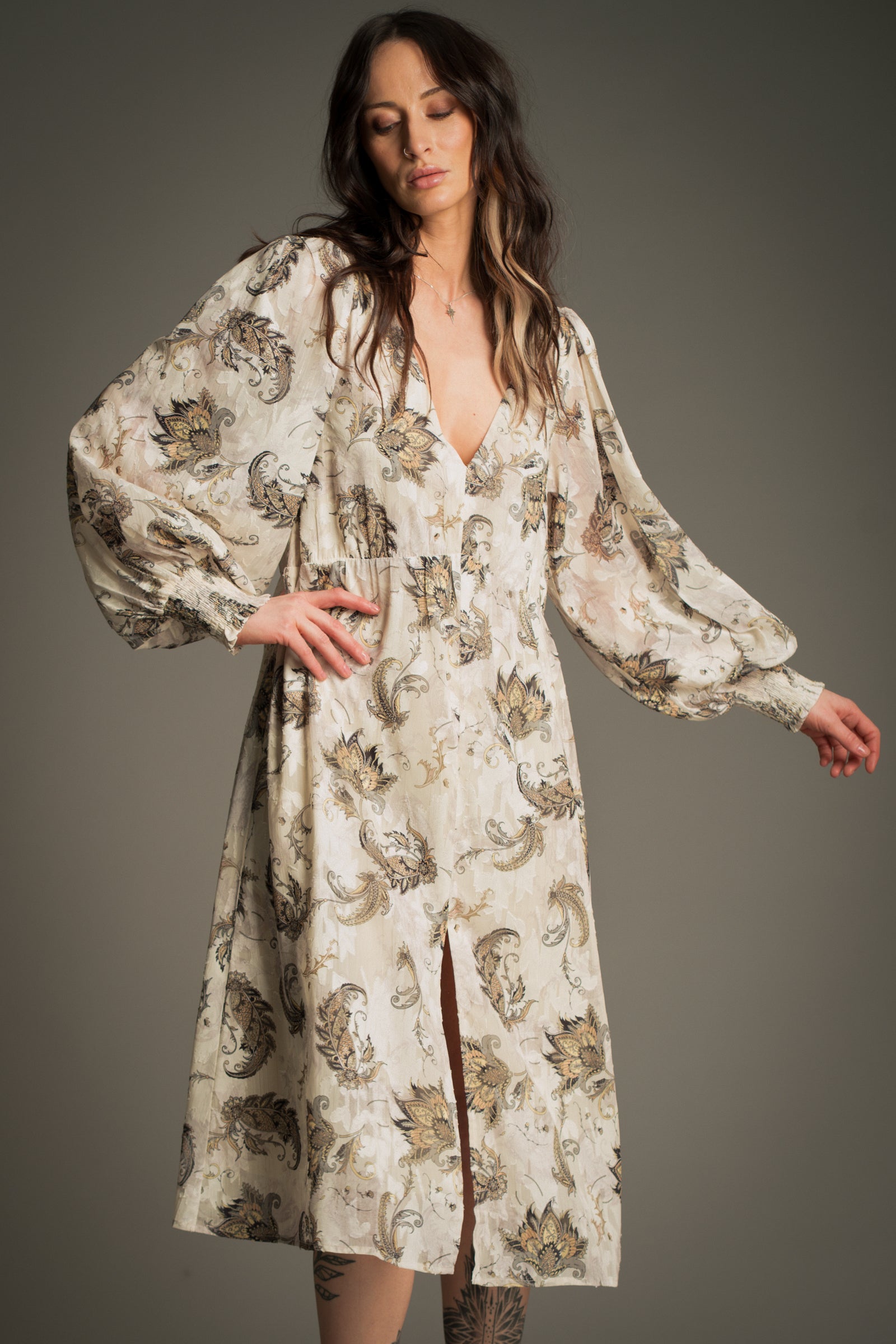 Victoria wears Little Lies Harvest Moon Paisley Midi Dress in cream with detailed paisley print, front view featuring long voluminous sleeves, deep V‑neckline, and front split hem.
