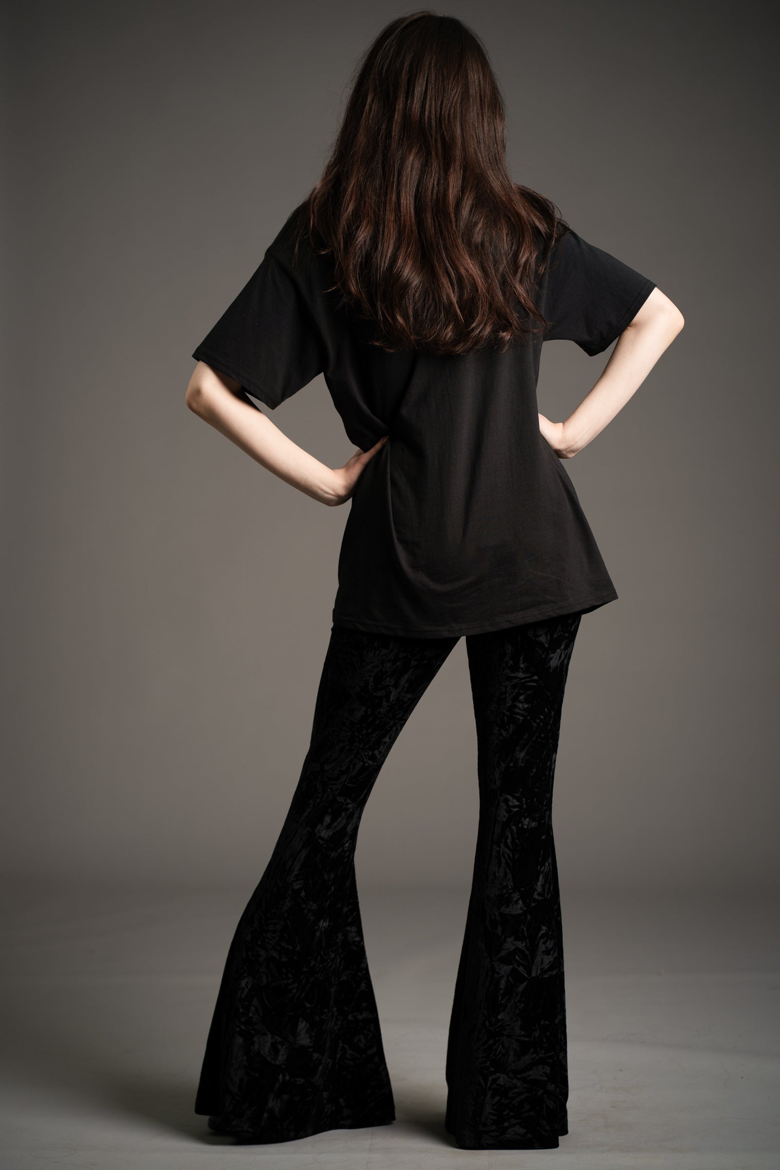 Little Lies Hendrix black crushed velvet flared trousers, back view showing dramatic bell-bottom silhouette, styled with oversized black tee in studio setting