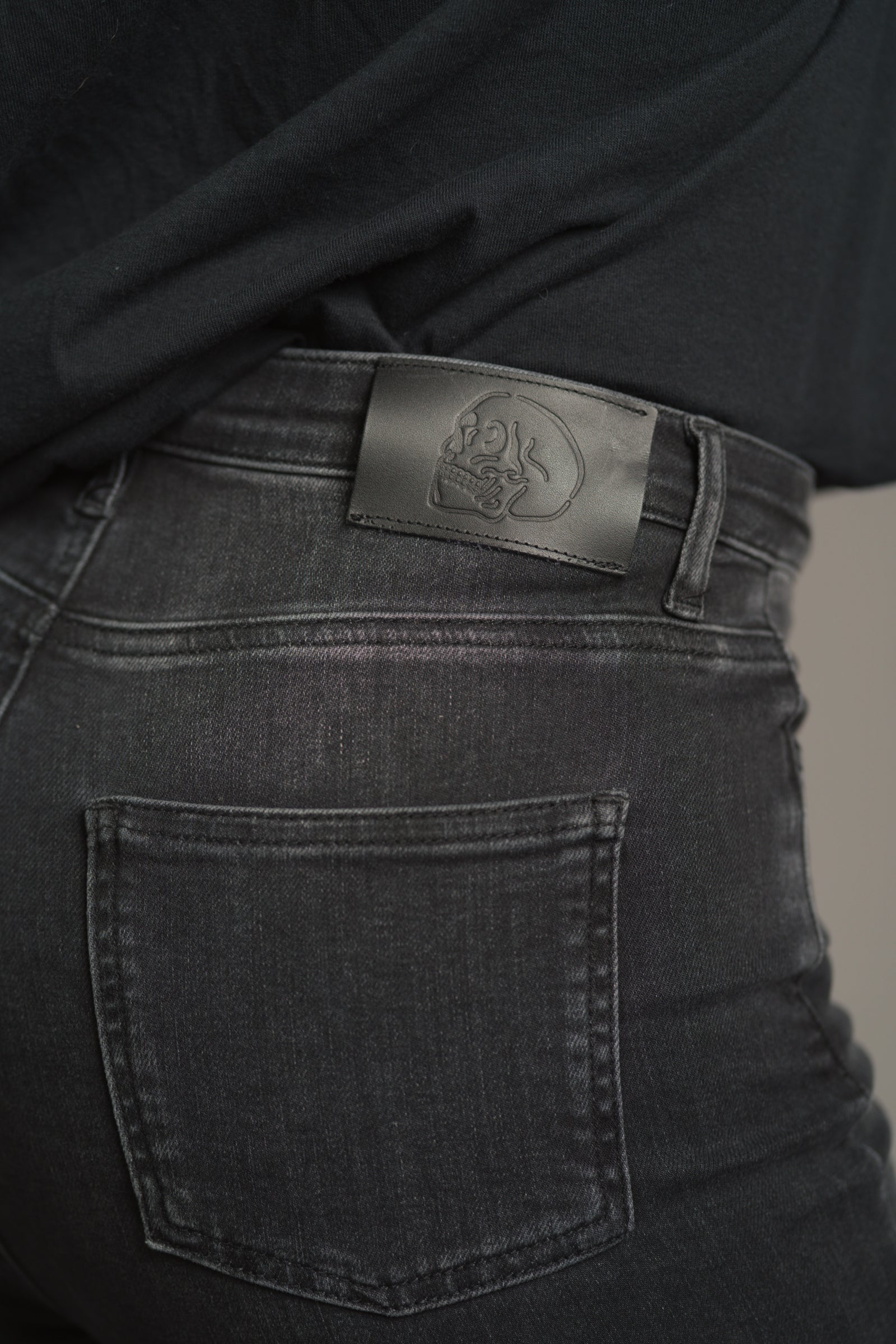 Close-up of embossed skull brand patch on Little Lies Hendrix Denim Flares – leather-look label stitched at the waistband with raised skull detailing.
