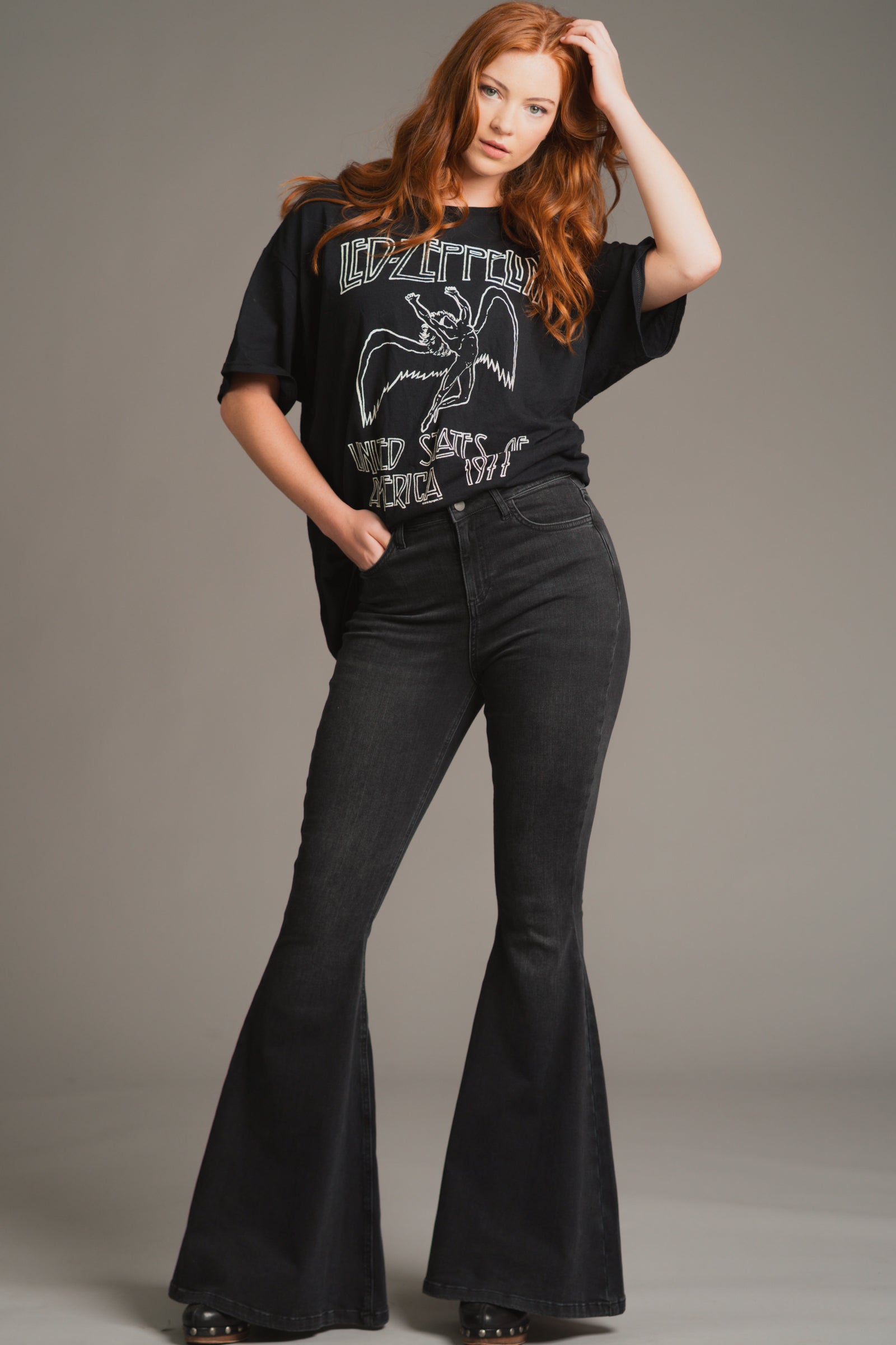 Anna wears Little Lies Hendrix Denim Flares with a vintage Led Zeppelin band tee – high-waisted denim flares styled with a bold graphic top for a rock-chic studio look, styled in a minimalist studio setting.
