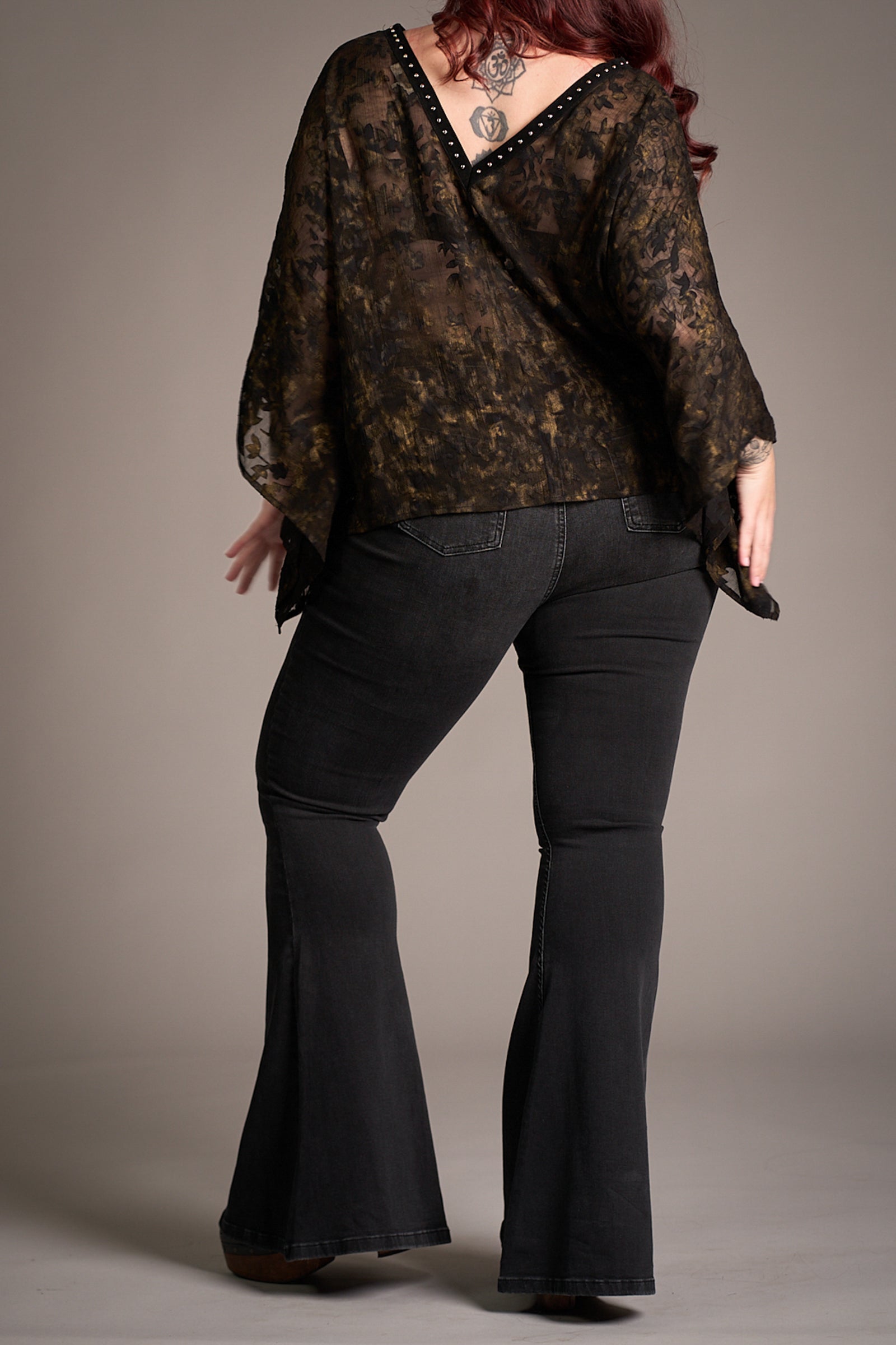 Back view of Taylor wearing Little Lies Hendrix Denim Flares and sheer lace Bella Donna Kimono – wide-sleeved top with studded V-back detail paired with dramatic flared denim, styled in a minimalist studio setting.