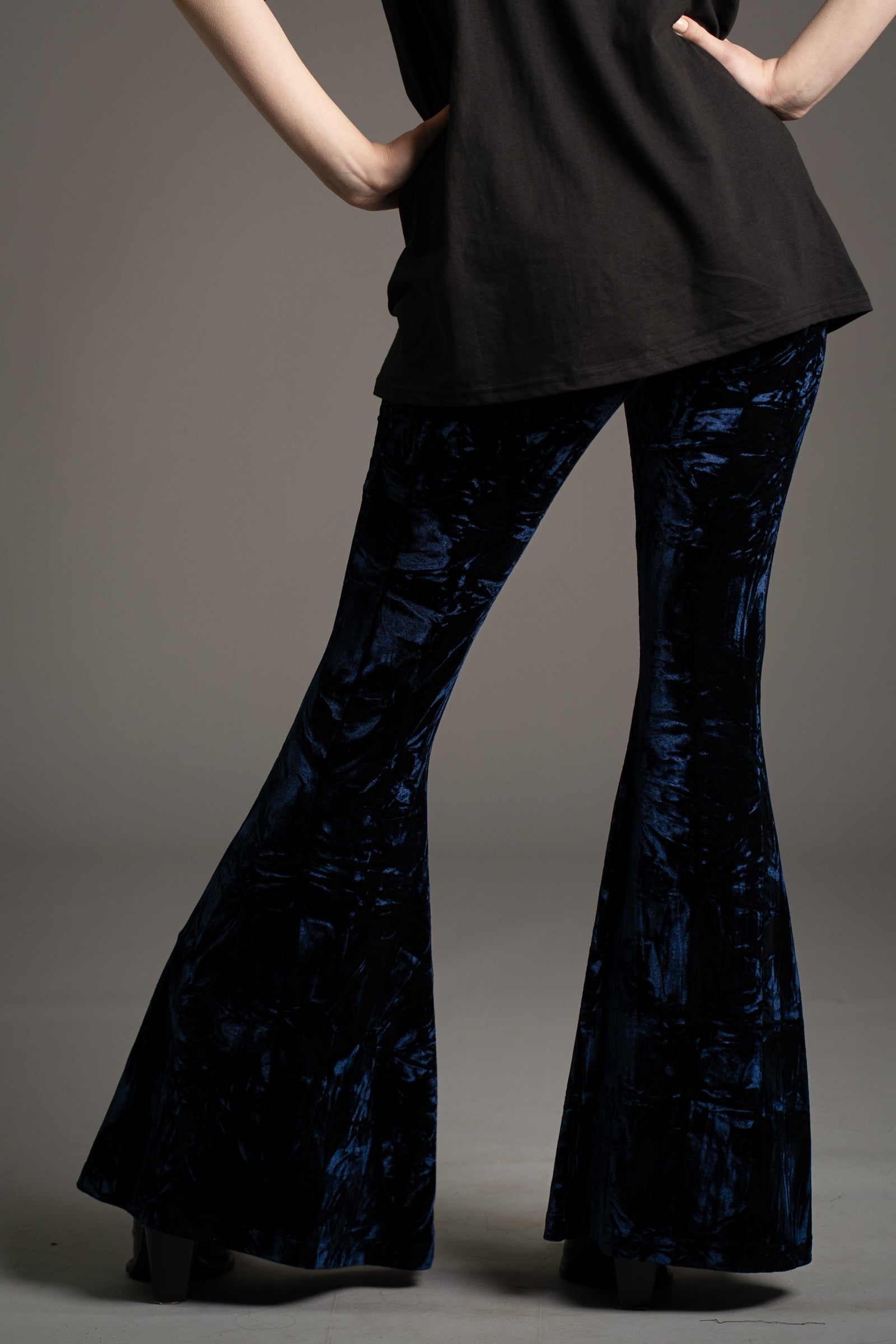 Back view of Little Lies crushed velvet flared trousers in deep midnight blue, styled with black graphic tee and boots