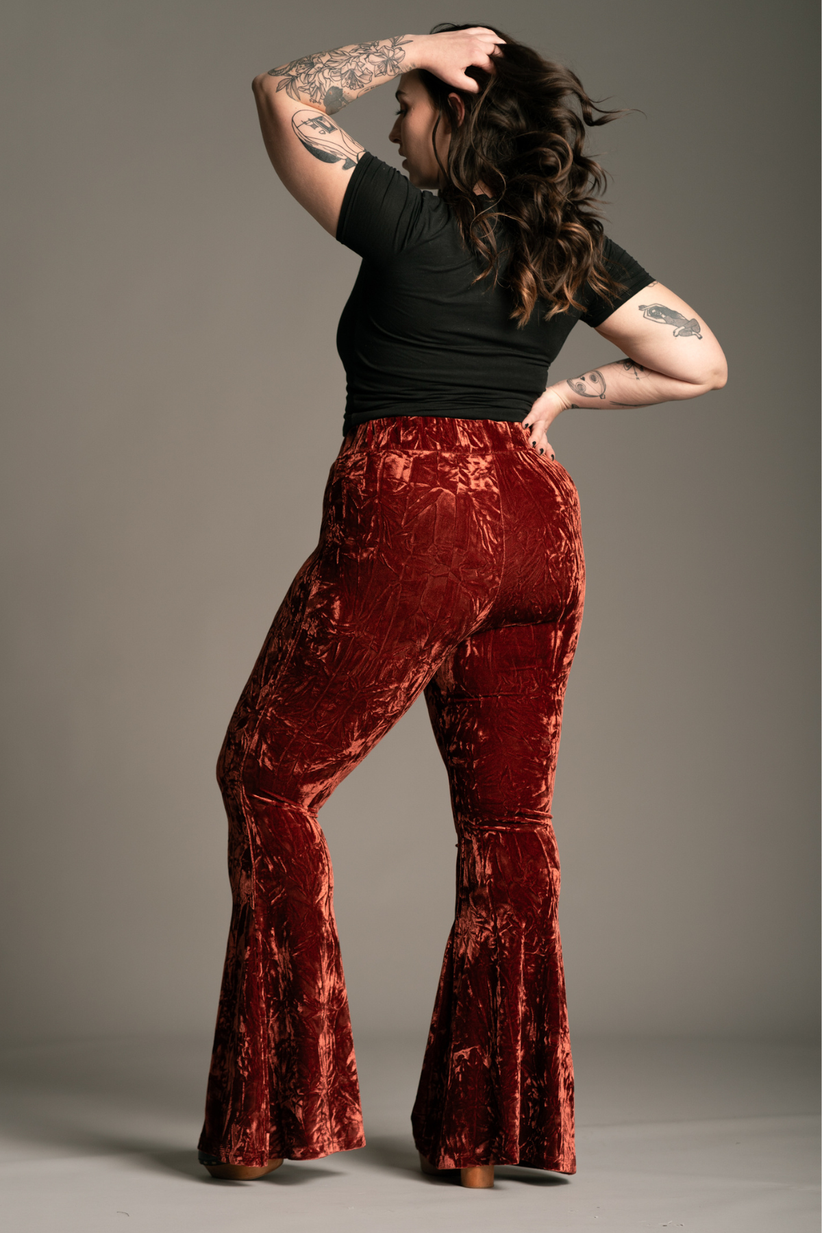 Model wearing Hendrix rust crushed velvet flare bell bottom trousers. styles with black tee.