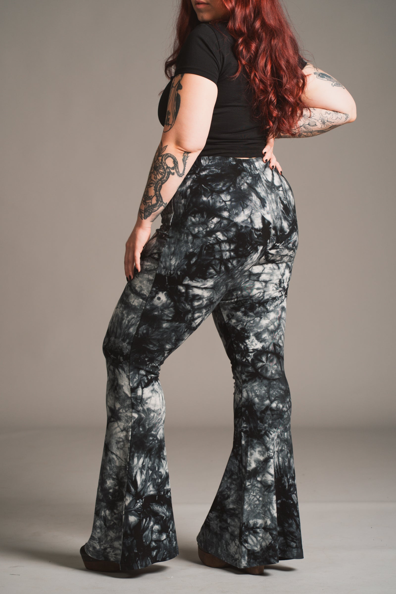 Taylor models Little Lies Hendrix tie dye flared trousers in black and grey styled with fitted black tee, side view studio shot