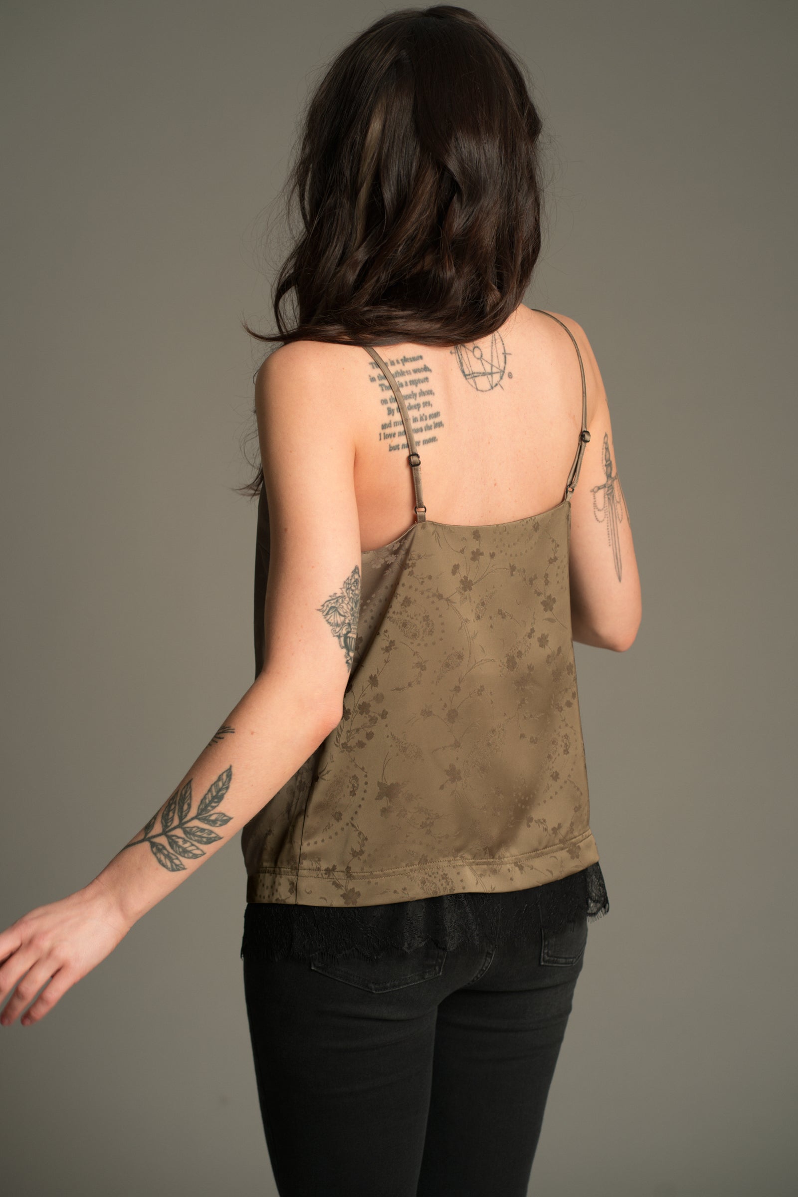 Back angled view of the Little Lies Iris Satin Cami in sage satin with tonal floral jacquard and black lace trim, styled with black jeans.