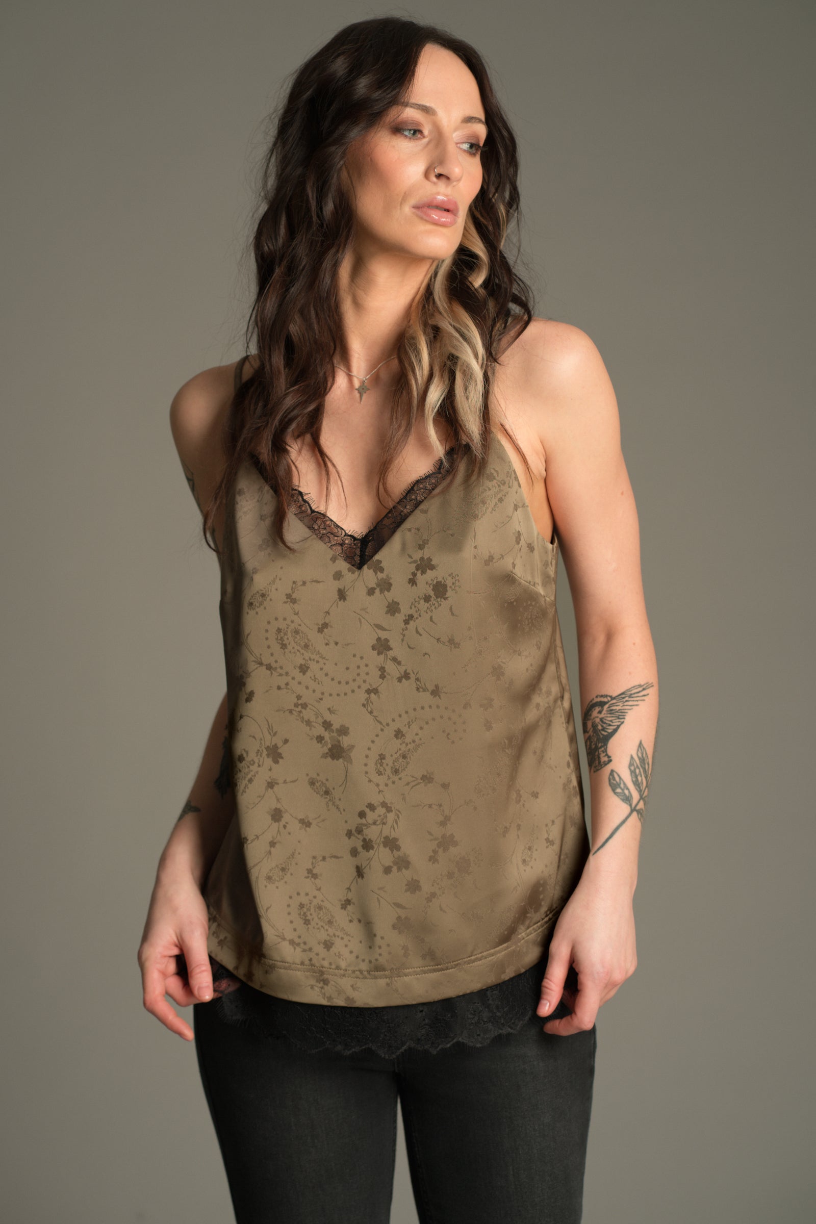 Front view of Victoria wearing the Little Lies Iris Satin Cami in sage satin with tonal floral jacquard and black lace trim, styled with black jeans.