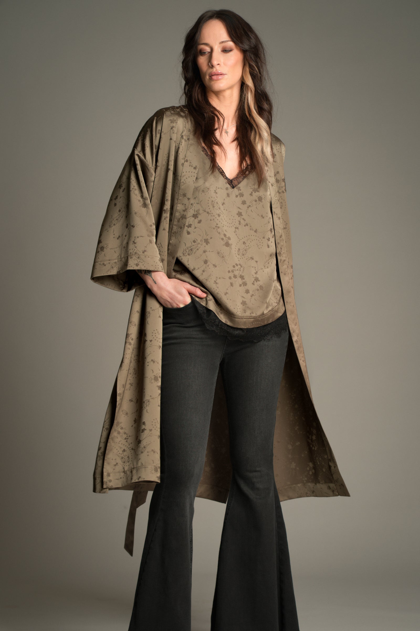 Front view of Victoria wearing the Little Lies Iris Satin Kimono in olive satin with a subtle floral jacquard pattern, layered over matching Iris Satin cami and styled with denim flared trousers.