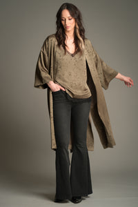 Front view of Victoria wearing the Little Lies Iris Satin Kimono in olive satin with a subtle floral jacquard pattern, layered over a matching Iris Satin cami and styled with denim flared trousers.