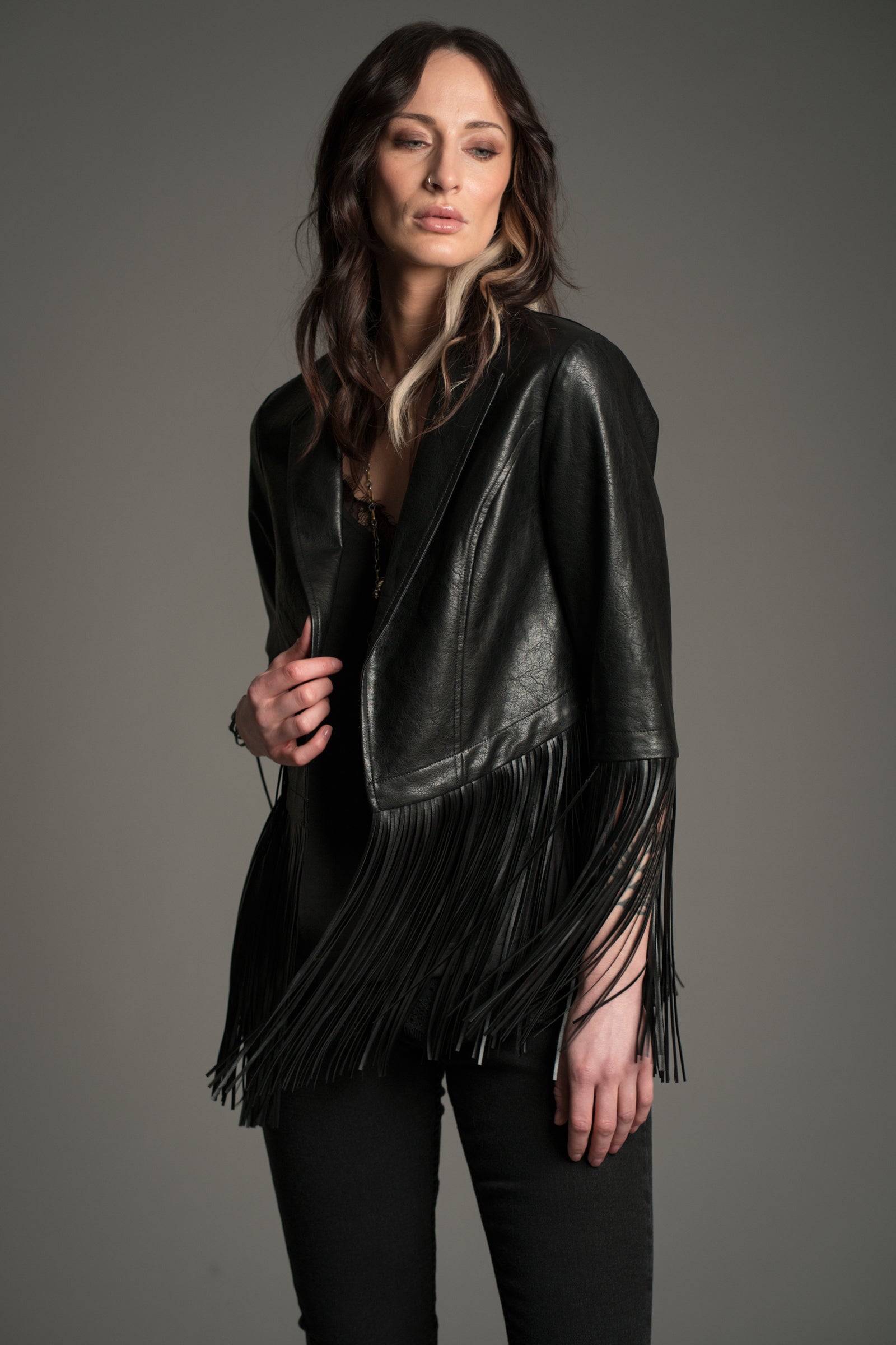 Victoria wears Little Lies Jagger Fringed Faux Leather Jacket in black, front view showing long dramatic fringe detailing on the sleeves and hem, styled with black denim.
