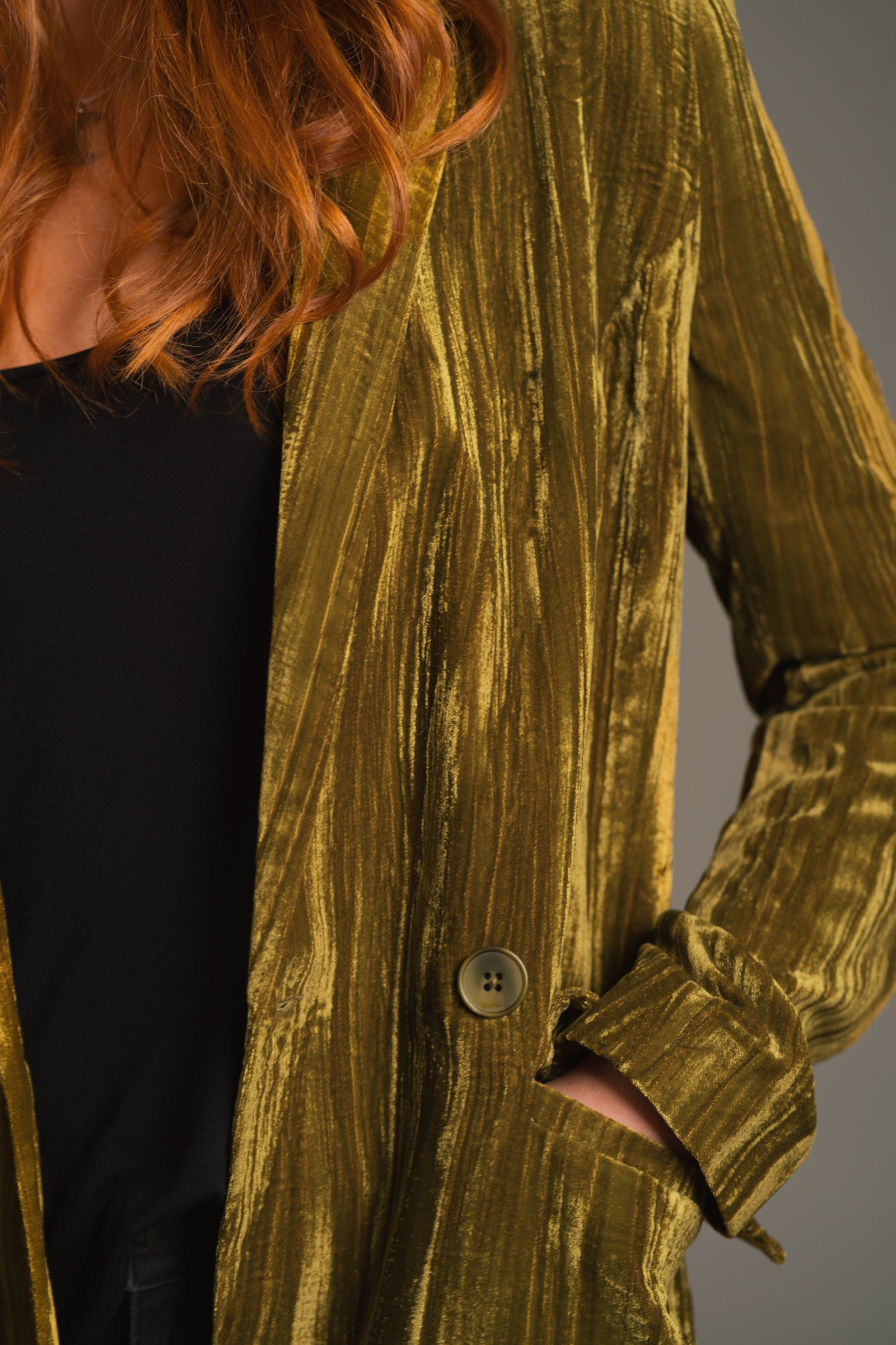 Close-up of slim lapel and button detail on rich olive crushed velvet fabric on the Jagger duster.