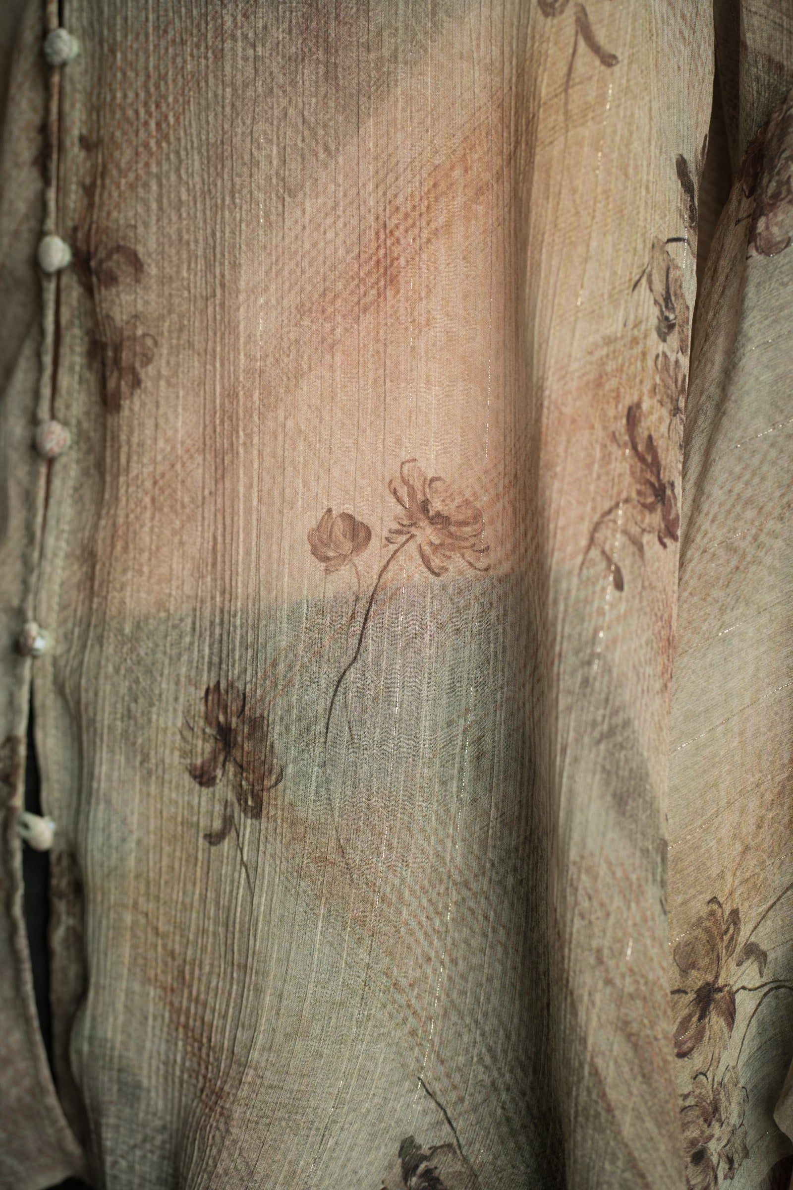 Close‑up of the Little Lies Karma Sage Blouse showing soft sage‑toned fabric with floral print, subtle shimmer, and covered button detail.
