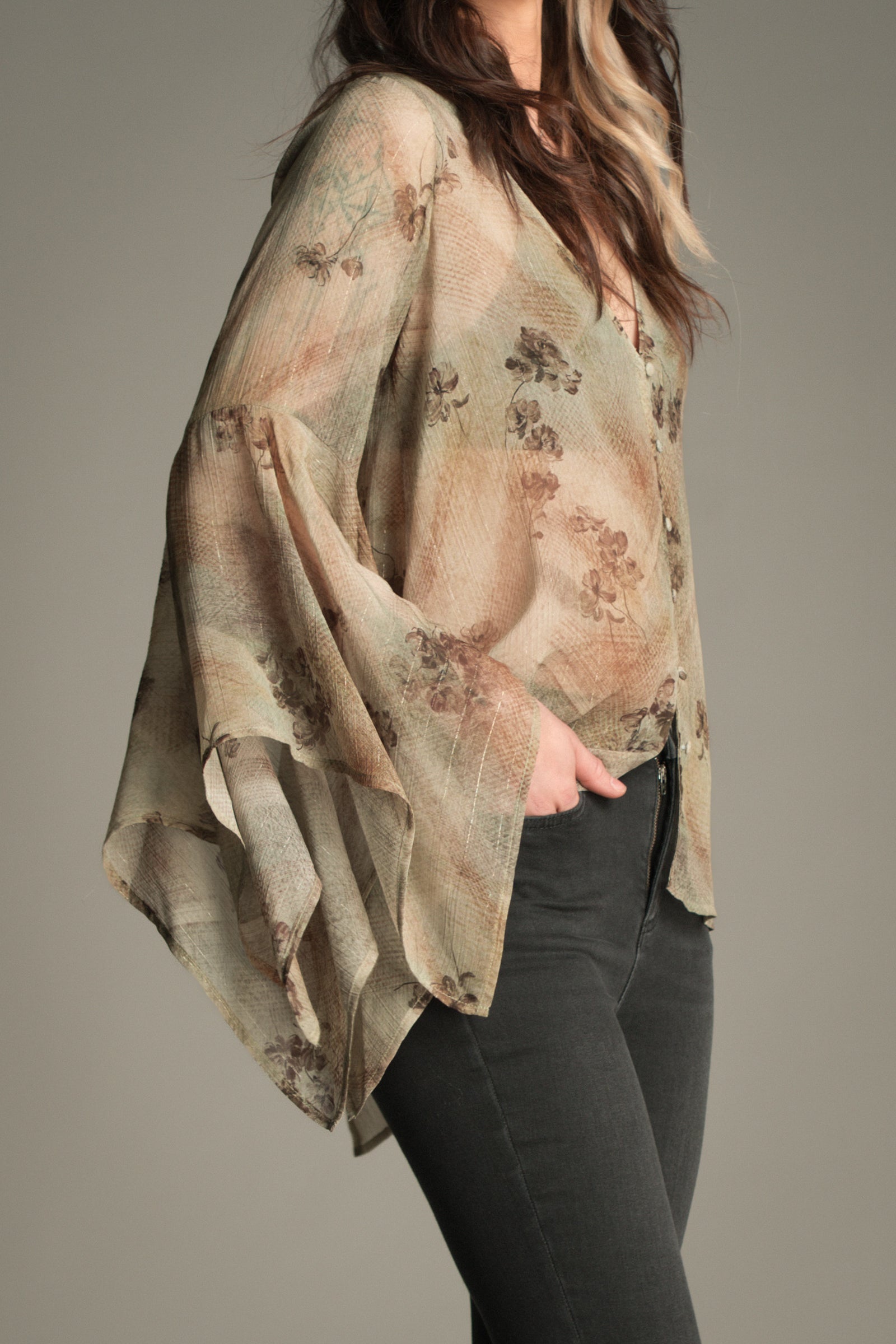 Side view of the Little Lies Karma Sage Blouse in soft sage floral print with flowing asymmetric sleeves, styled with high‑waisted flared trousers