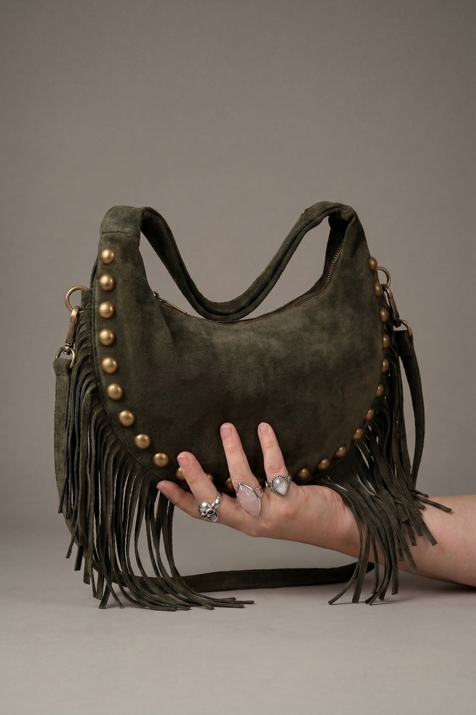 Kate Green suede handbag with gold studs and fringe held by a model.
