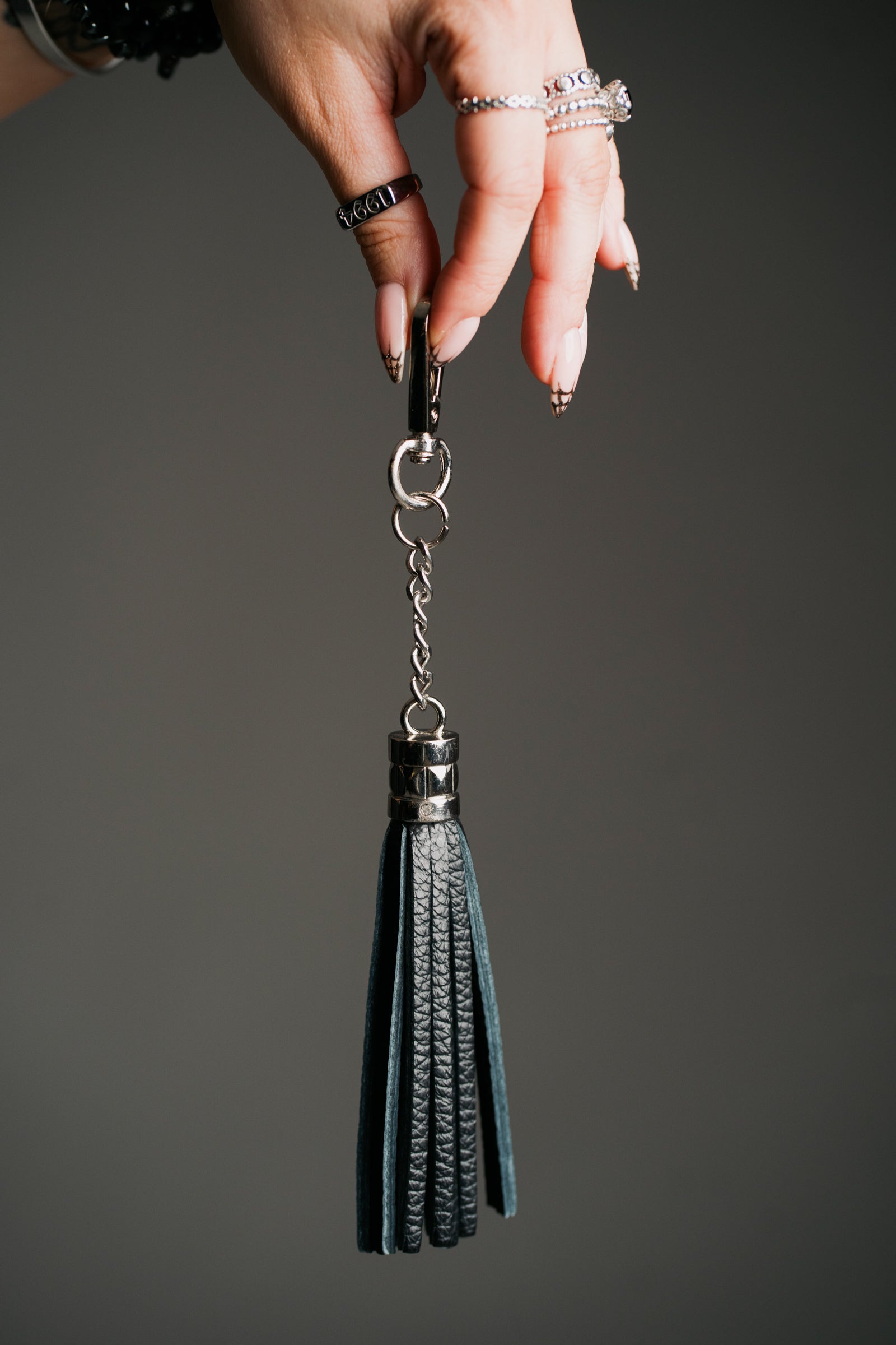 A black genuine leather tassel bag charm / keyring hanging on a dark background.