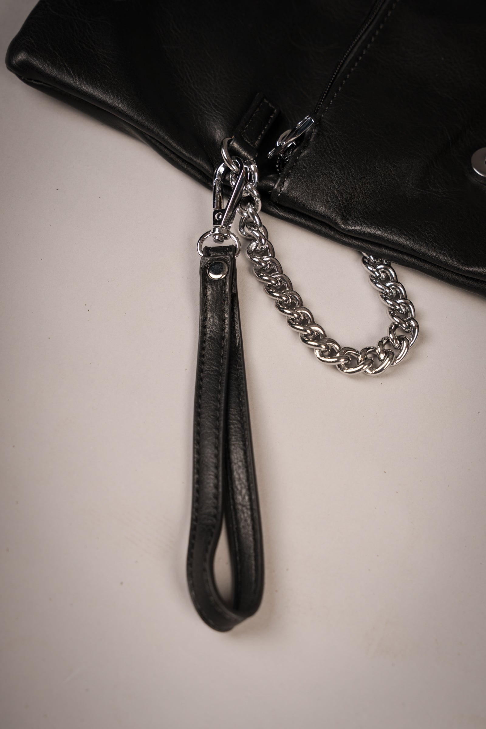 Close-up of Little Lies Zoë studded black faux leather clutch showing detachable wrist strap and silver-tone chain detail, studio setting