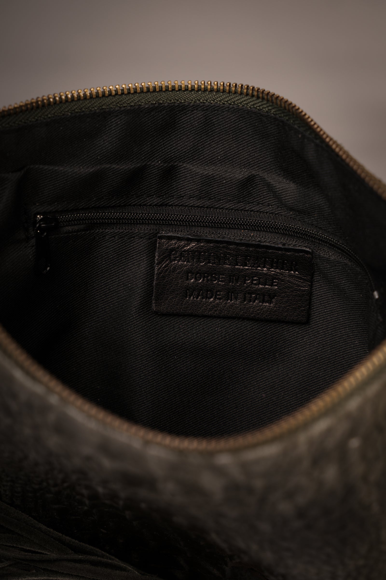 Close-up of interior of Little Lies Niska Khaki Genuine Suede Fringed Bag showing black fabric lining and zip pocket with Genuine Leather label