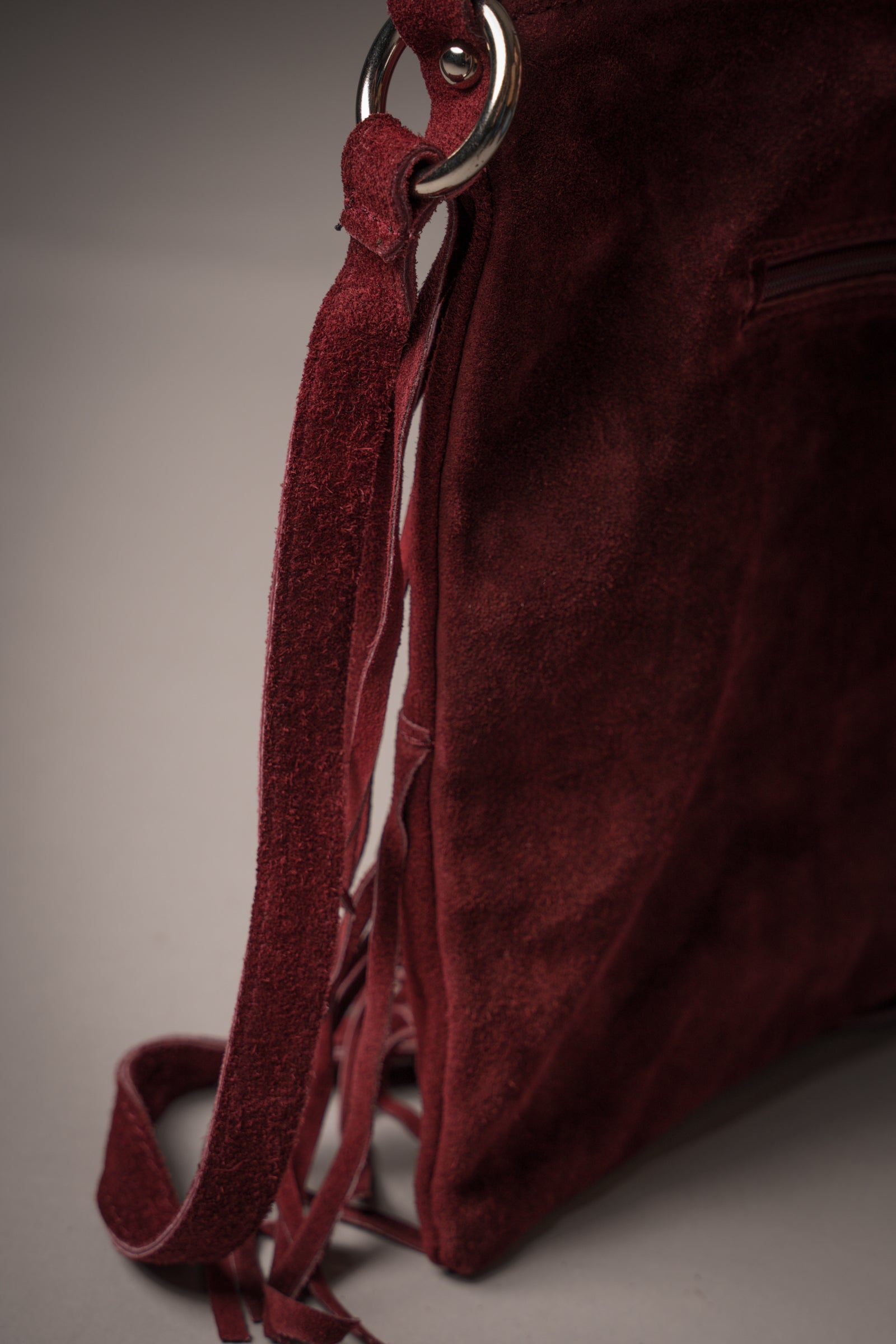 Close-up of Little Lies Oxblood Genuine Suede fringed bag showing detailed tassel design and shoulder strap with silver hardware, studio setting