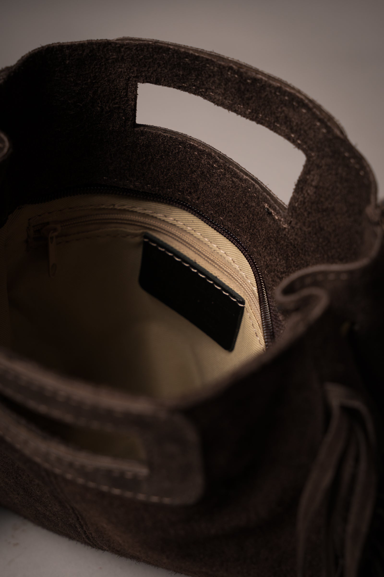 Interior view of Little Lies Annabella Chocolate genuine suede handbag showing beige lining, zip pocket, and cut-out handle detail, studio setting