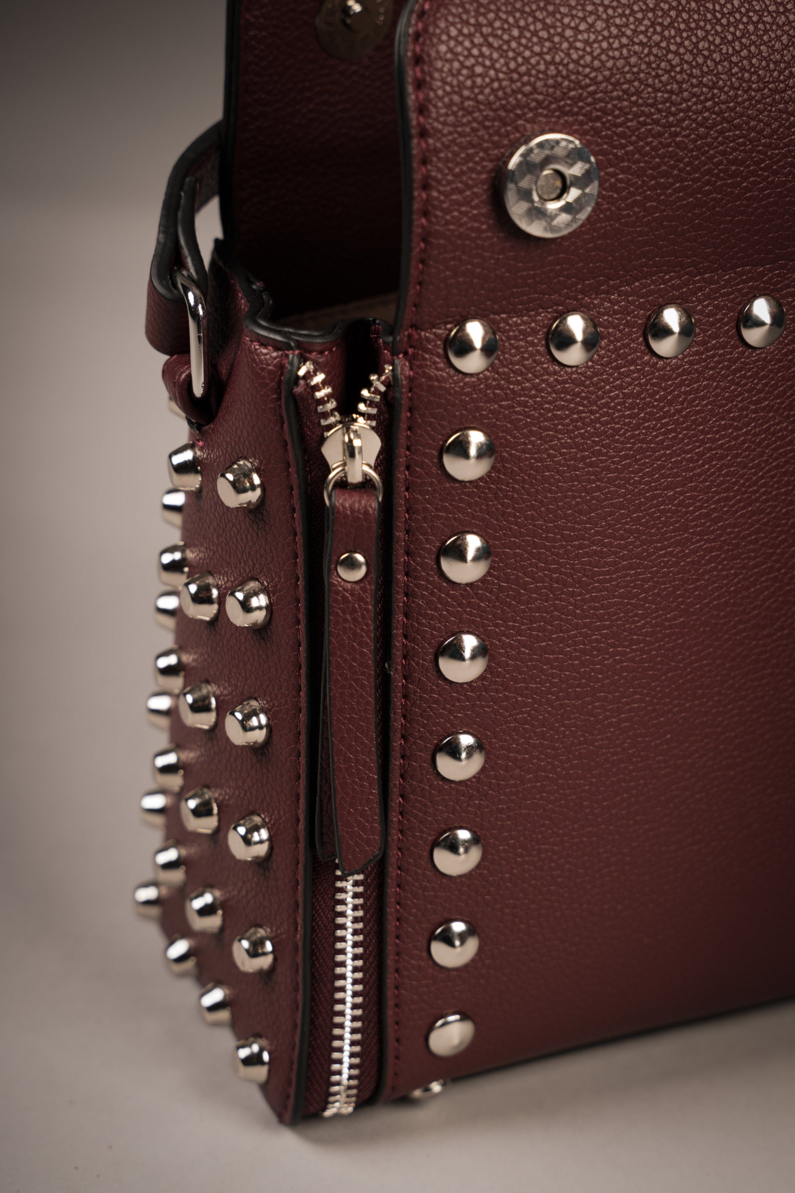 Little Lies Leo Burgundy studded box bag close-up showing zip detail, silver studs, and magnetic snap opening