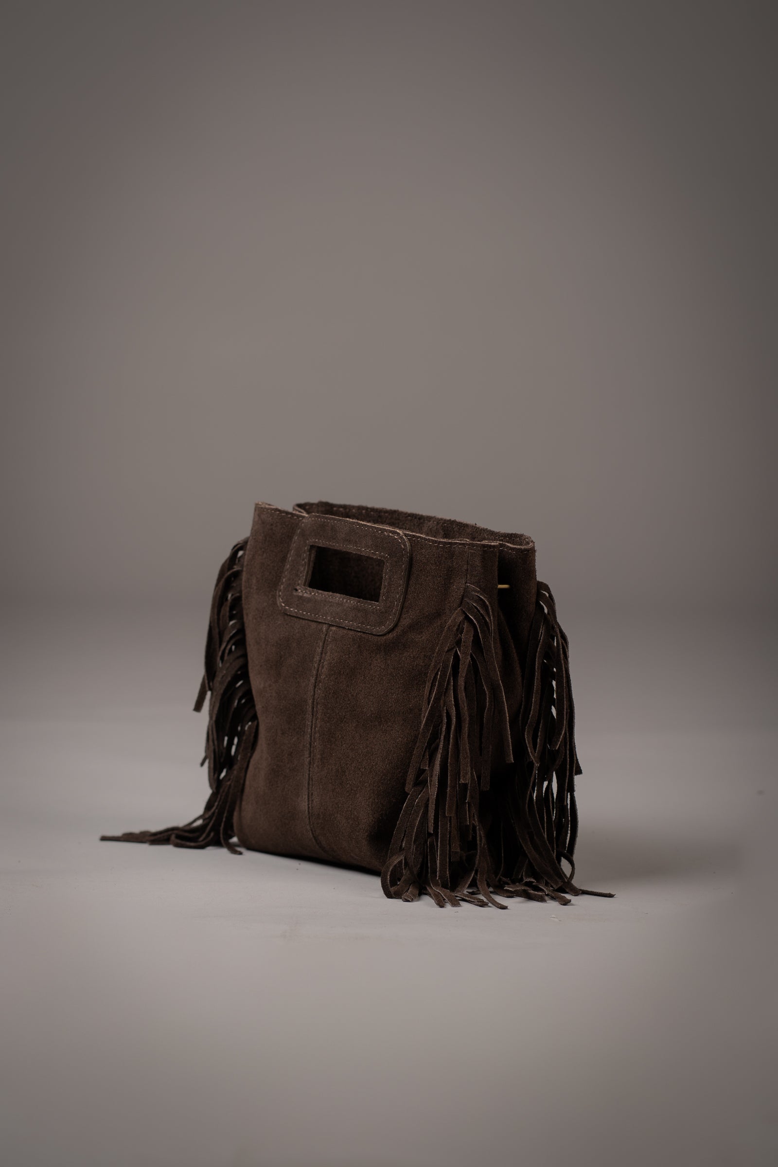 Little Lies Annabella Chocolate genuine suede handbag with fringe detailing and cut-out handle, photographed in a studio setting
