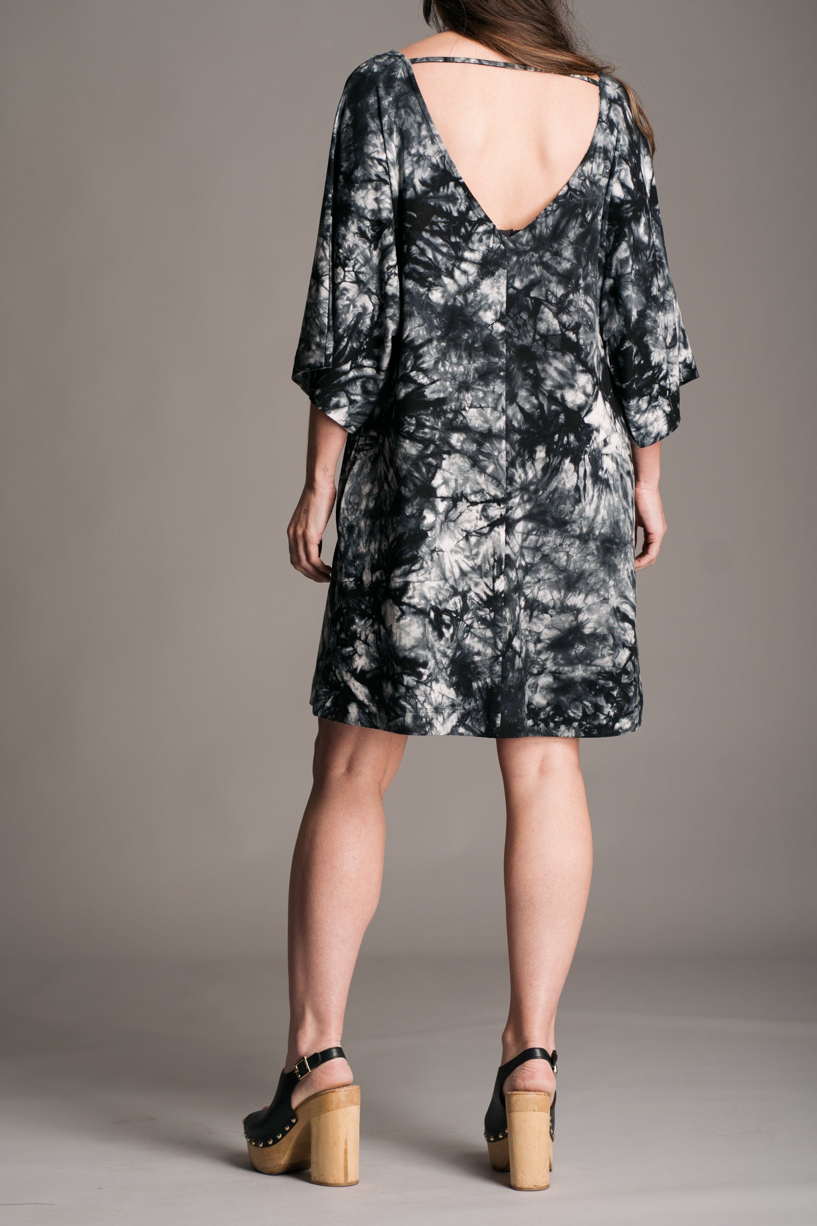 Joplin Tie Dye Mini Dress worn onset by brunette model, Bex, also wearing black leather wooden clogs. Showing the back of the dress