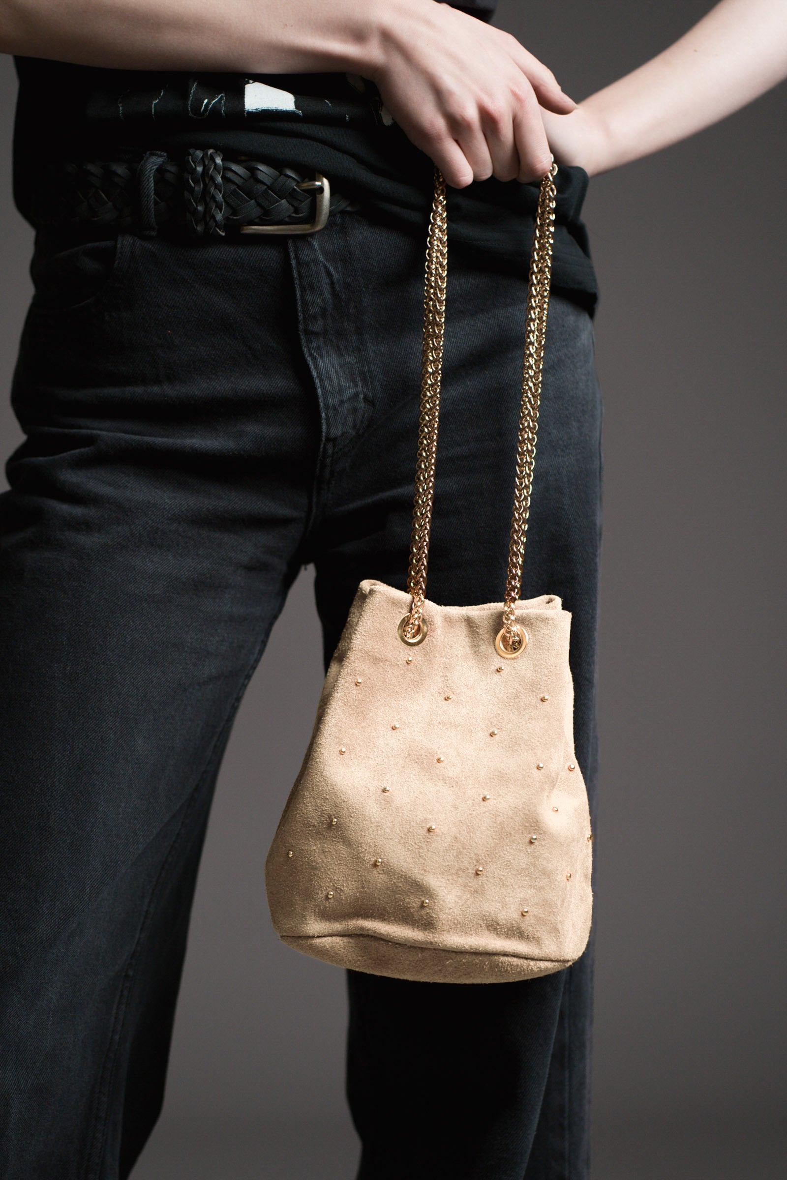 Model carrying the Lola Genuine Suede Studded Bucket Bag with a dark background