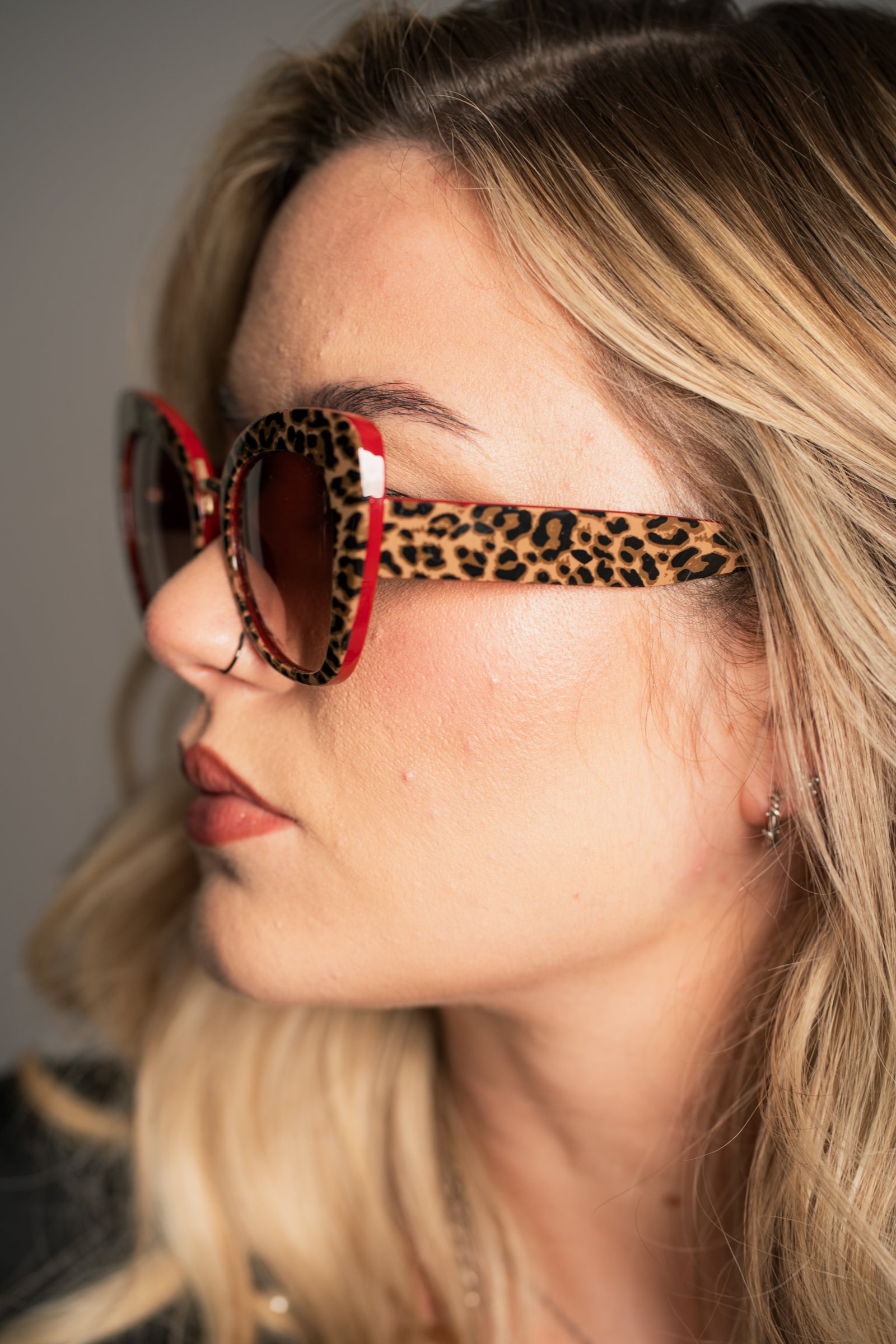 Little Lies Lola retro leopard print sunglasses with red frame detail and brown tinted lenses, oversized statement frame, side close‑up view