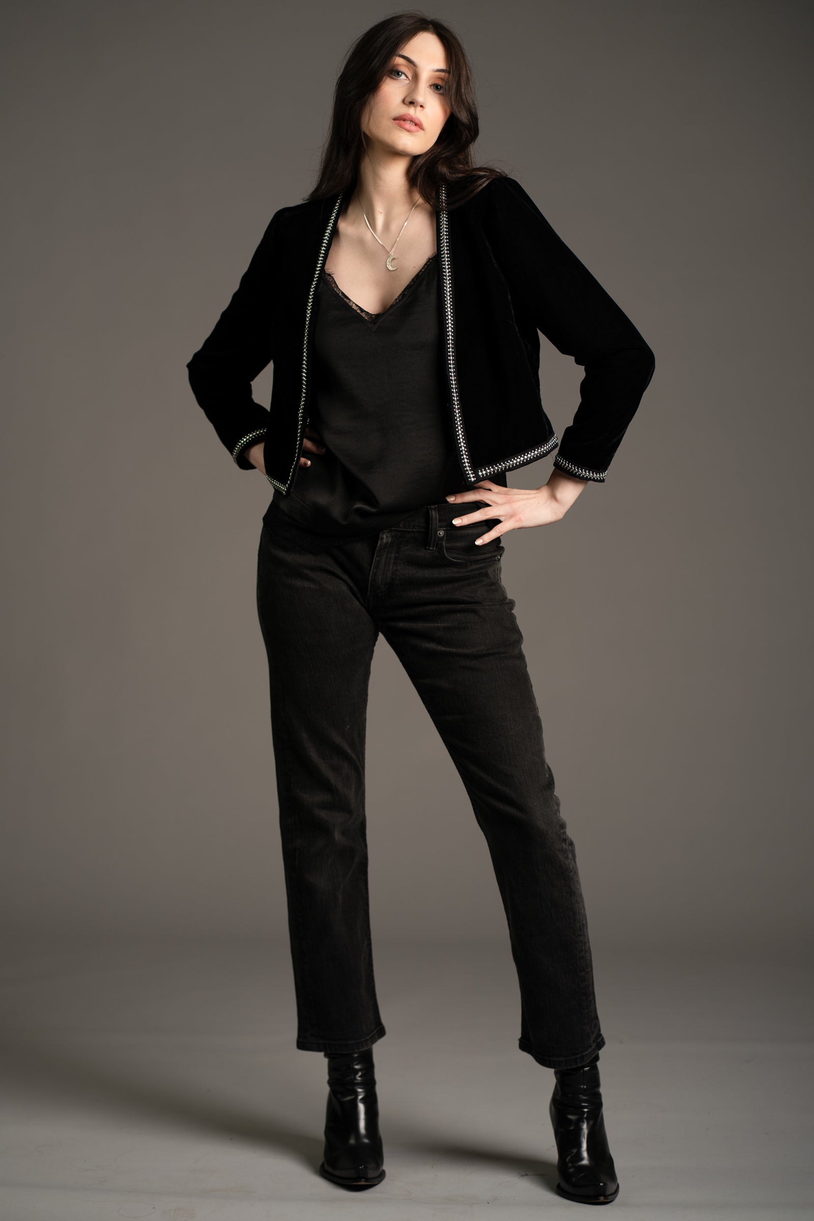 Andie models Little Lies Metal Guru studded velvet jacket in black, styled with black lace camisole, straight-leg dark jeans, and black ankle boots in studio setting
