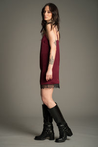 Victoria posing against a grey studio backdrop, wearing the Little Lies Nightbird Plum Satin Slip Dress Mini showing the side of the dress with lace trim hem