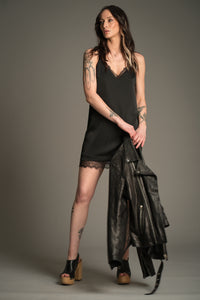 Victoria posing in black Nightbird Satin mini dress with lace trim neckline and hem, styled with wooden heeled clogs and leather biker jacket