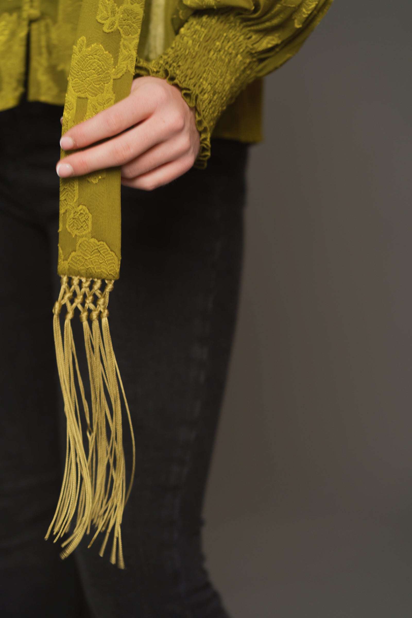Close-up of fringed end detail on olive chiffon skinny scarf with sheer texture