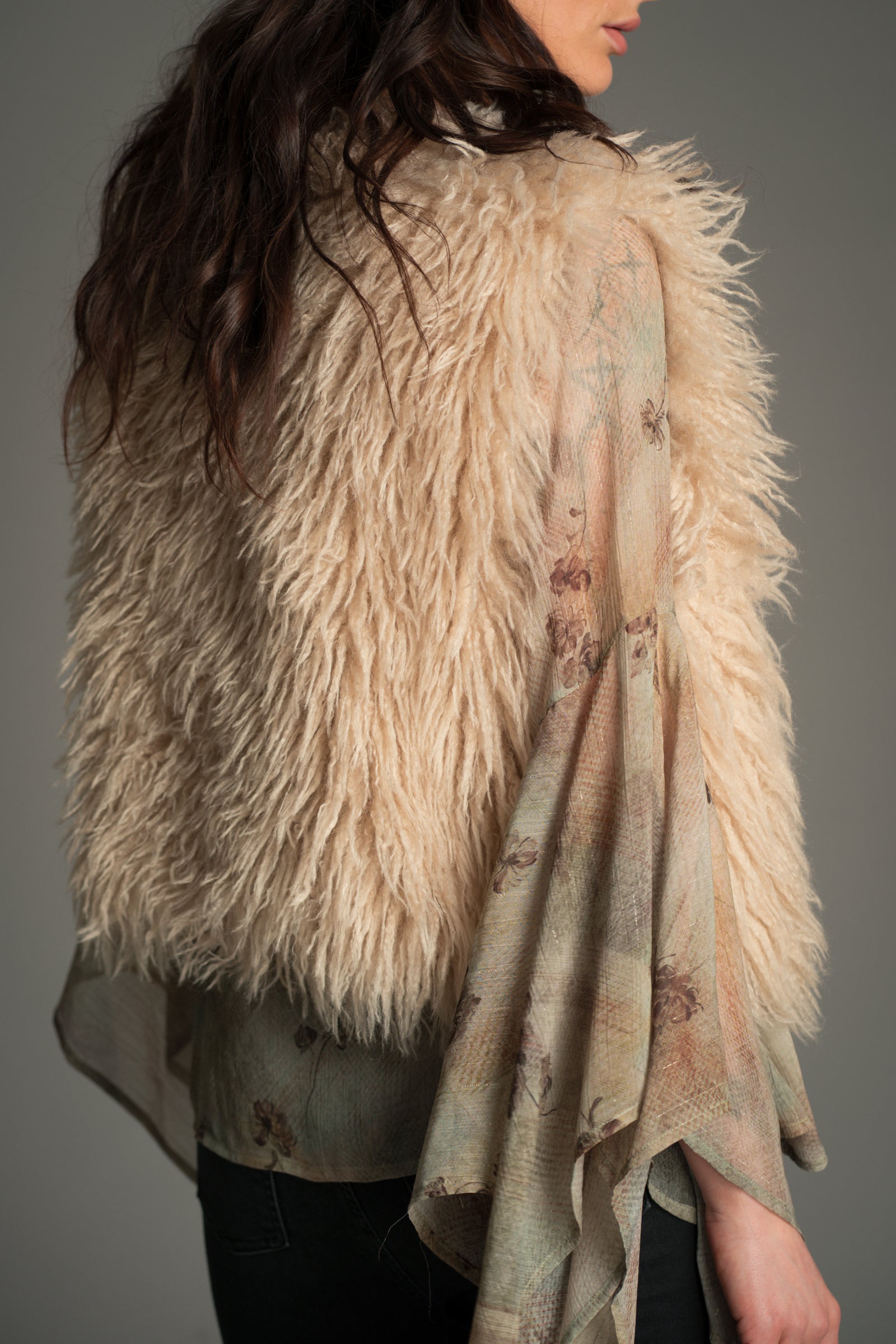 Back view of model wearing the beige faux‑fur Little Lies Penny Lane gilet layered over a sheer floral blouse with wide draped sleeves.