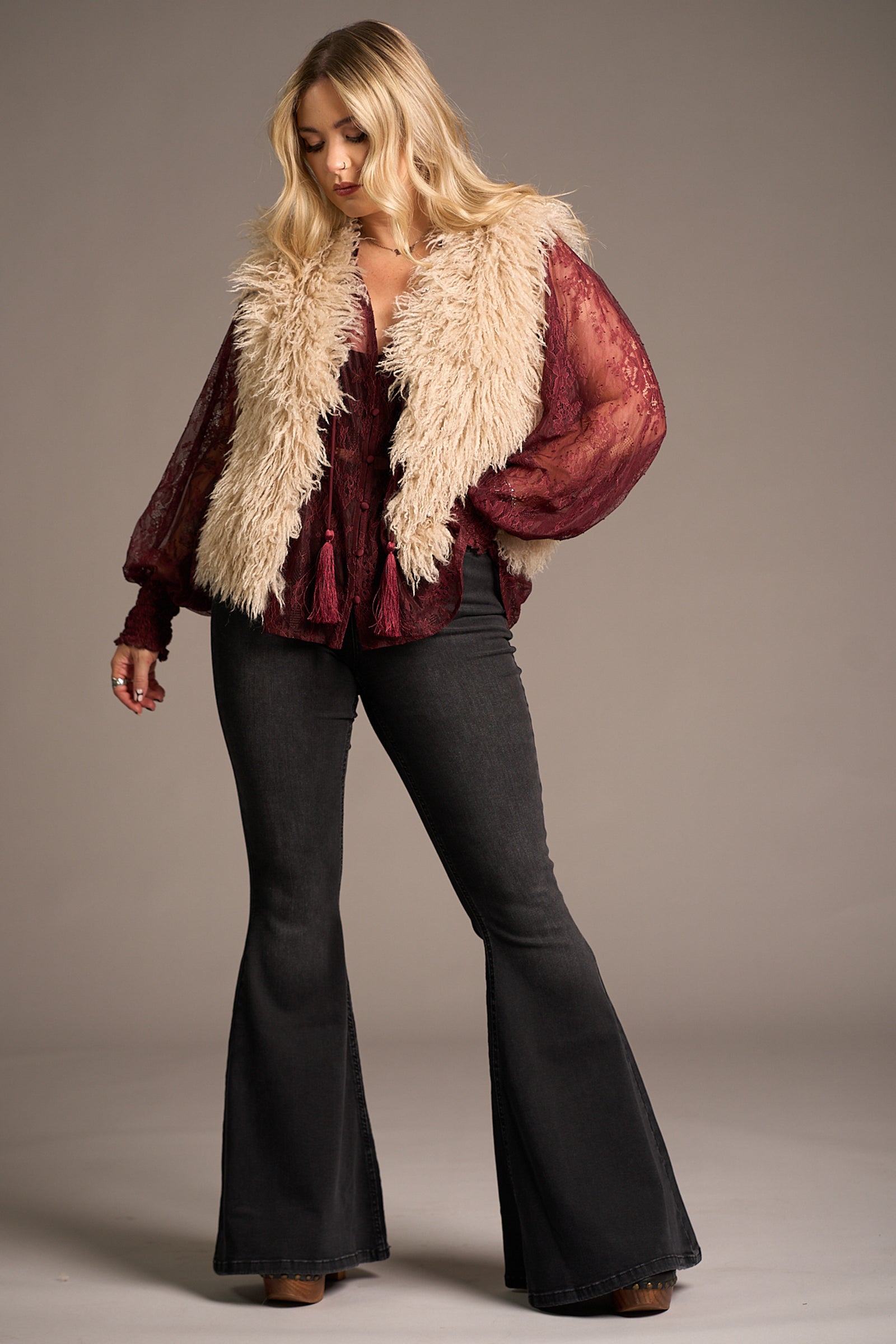 Erin wears cream Penny Lane Faux Mongolian Fur Gilet over burgundy lace blouse and flared jeans