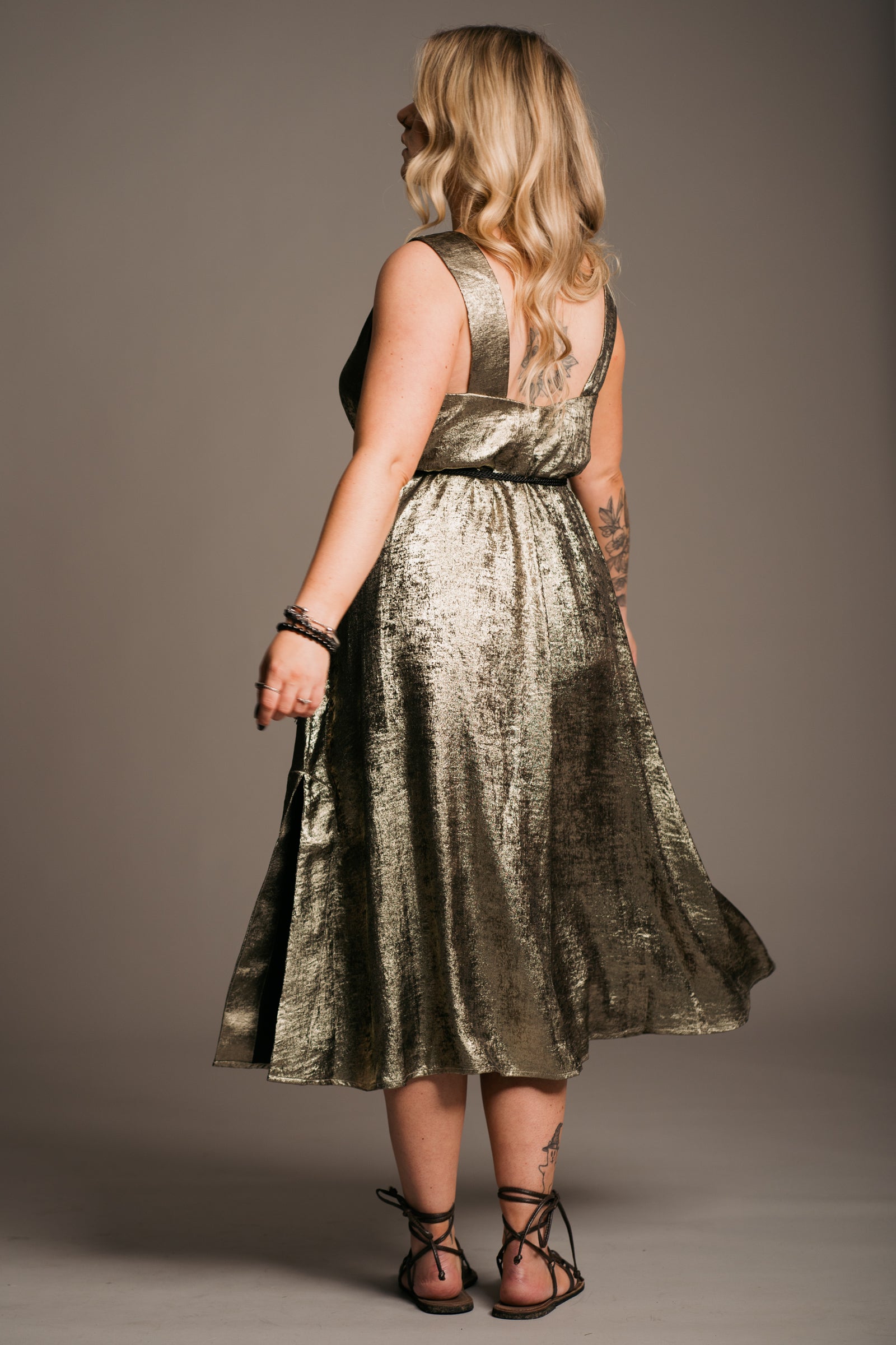 Blonde model in front of a grey backdrop in studio. Erin is wearing the Little Lies Ramble on Gold metallic Midi Dress, tie sandals and Little Lies Crescent Moon Necklace