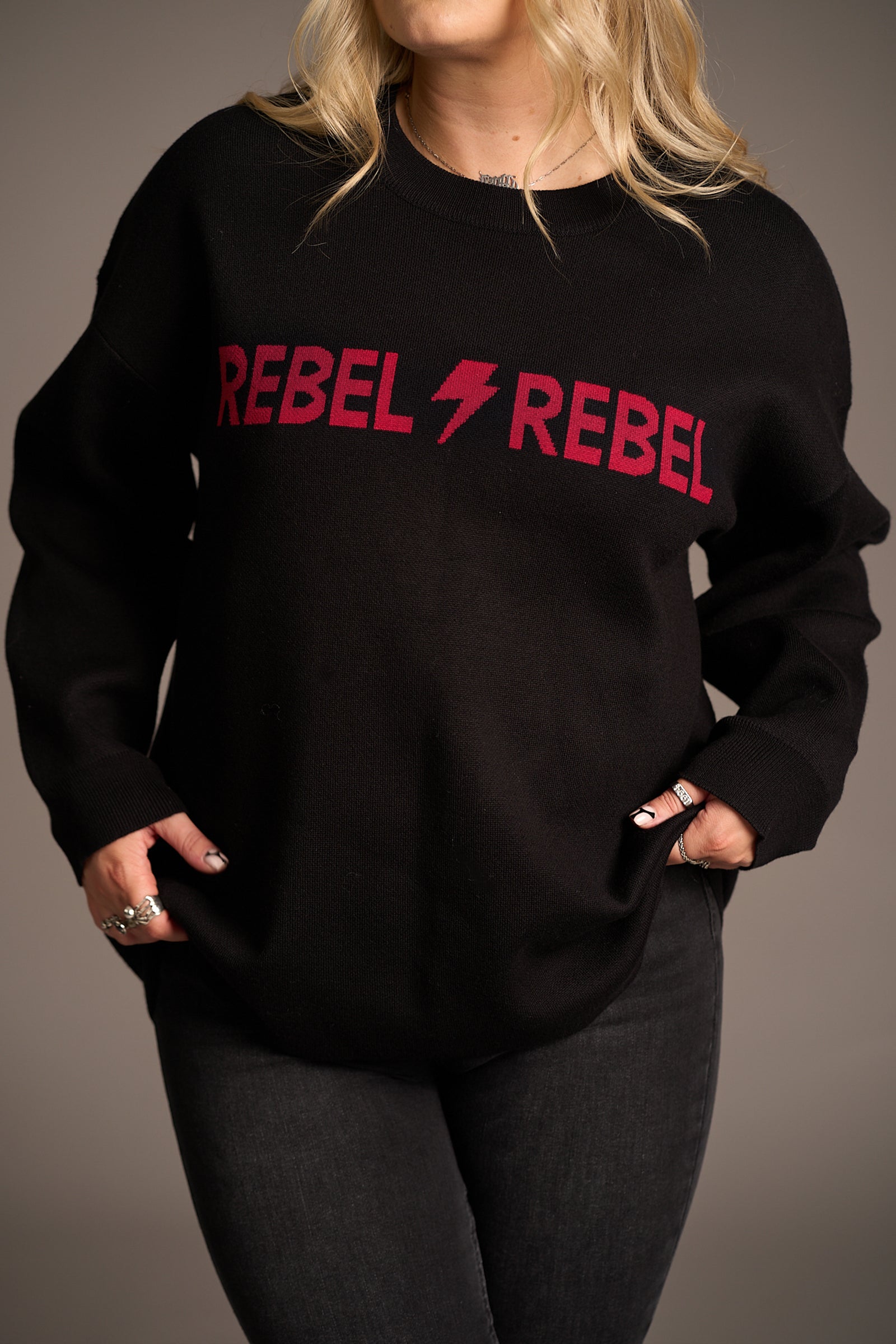 Close-up of “Rebel Rebel” slogan on Little Lies Red Knit Jumper – bold red lettering with lightning bolt graphic on black knit, capturing a rebellious retro vibe.
