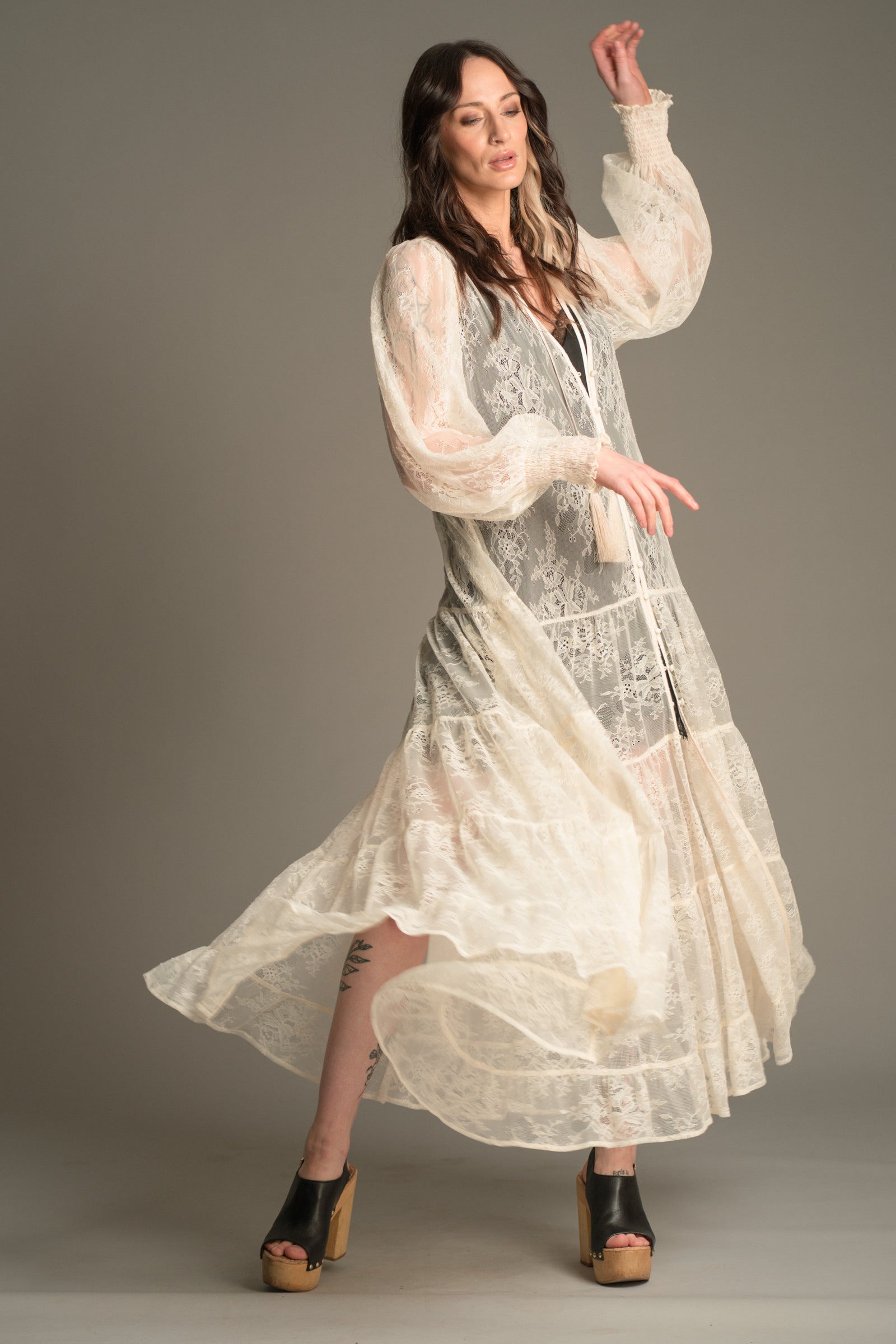 Flowing action shot of Victoria wearing the Little Lies Rhiannon Ivory Maxi Dress in sheer ivory lace, featuring long voluminous sleeves, tassel ties, and a tiered maxi‑length skirt in motion.