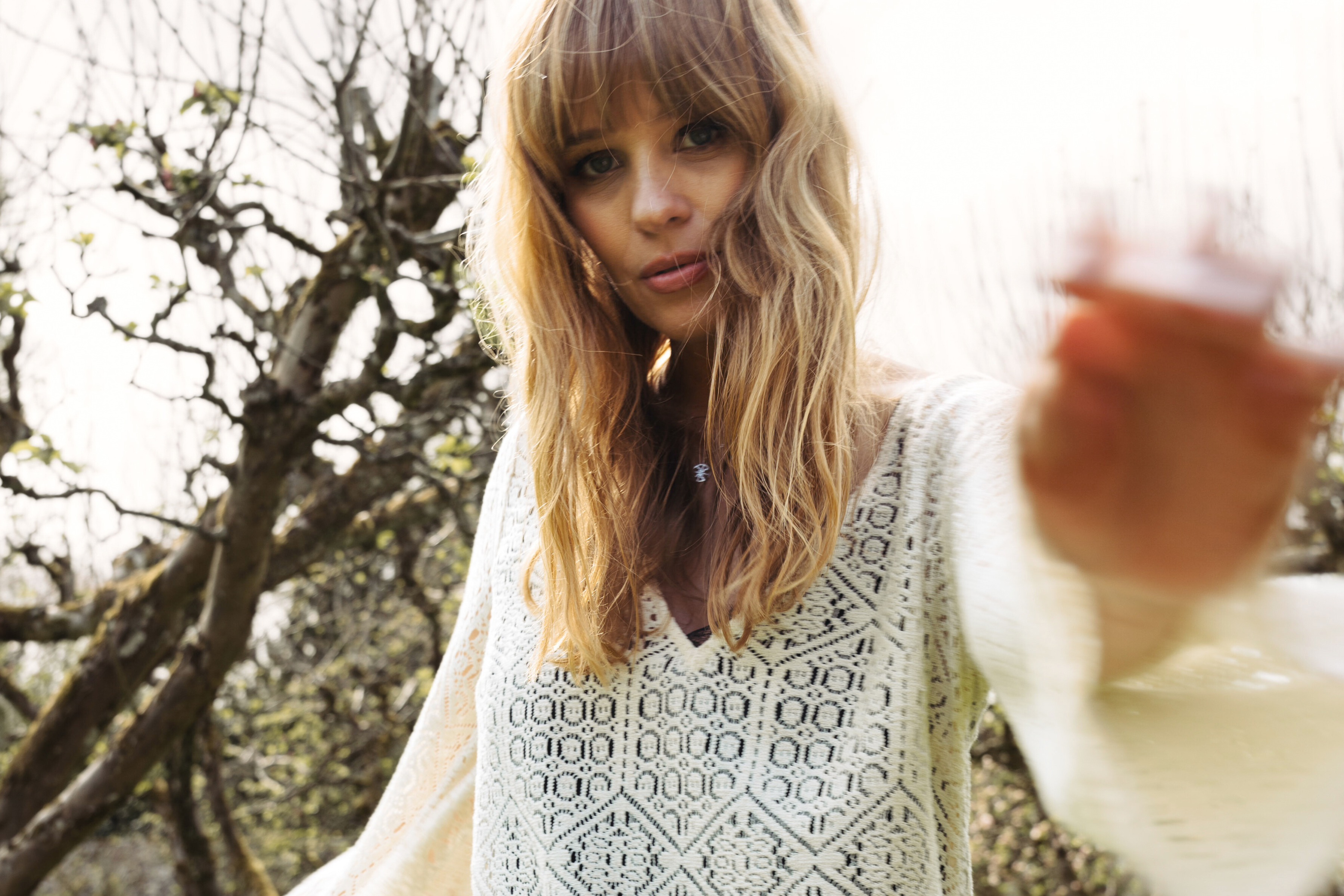 Model Tinna in Little Lies Goldie Ivory Crochet Mini Dress with flared sleeves, posing in a festival setting.