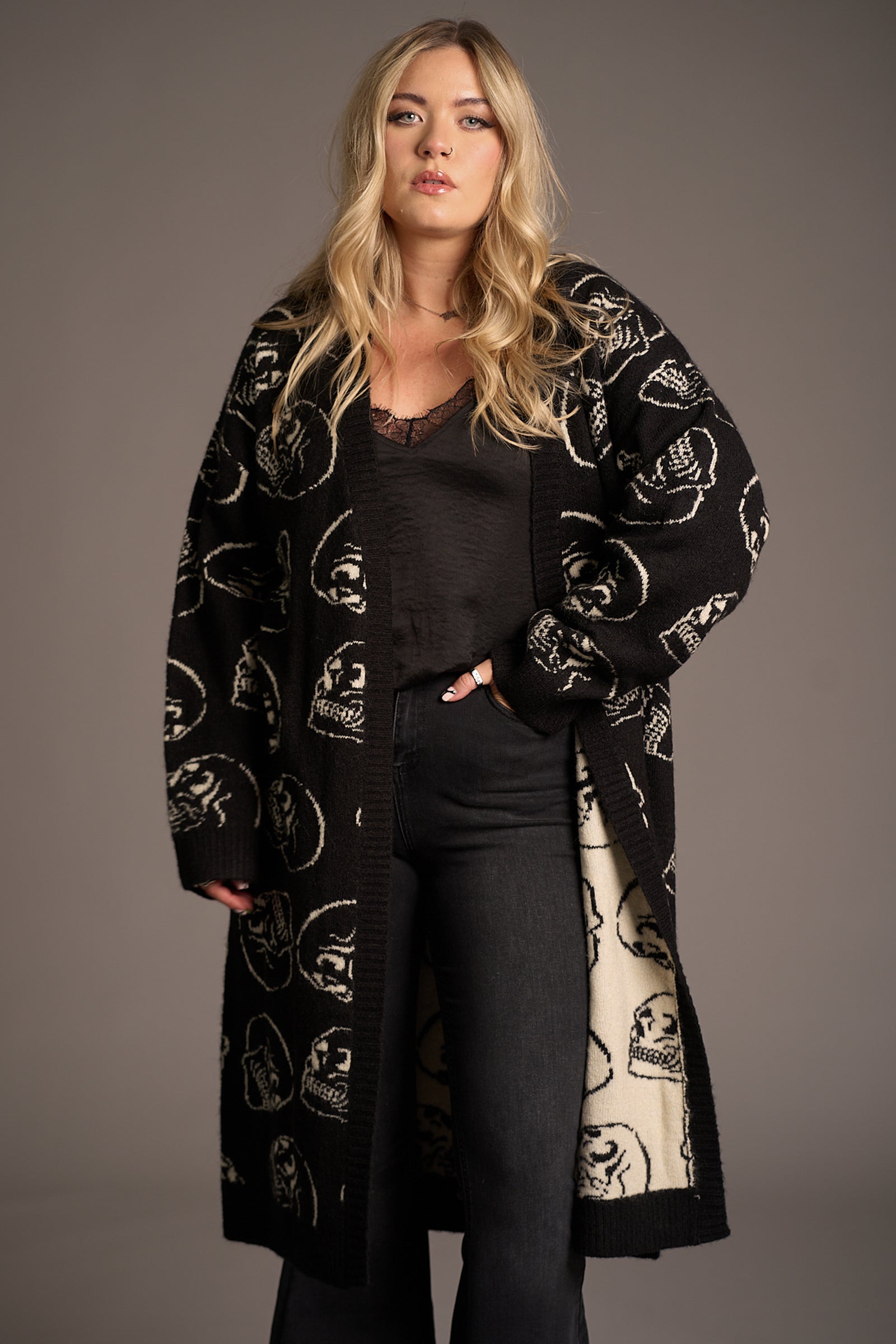 Front view of Erin wearing the Little Lies Skull Knit Cardigan – styled to reveal the light reverse side with inverted skull motifs, showcasing the dual-tone design and graphic impact in studio.