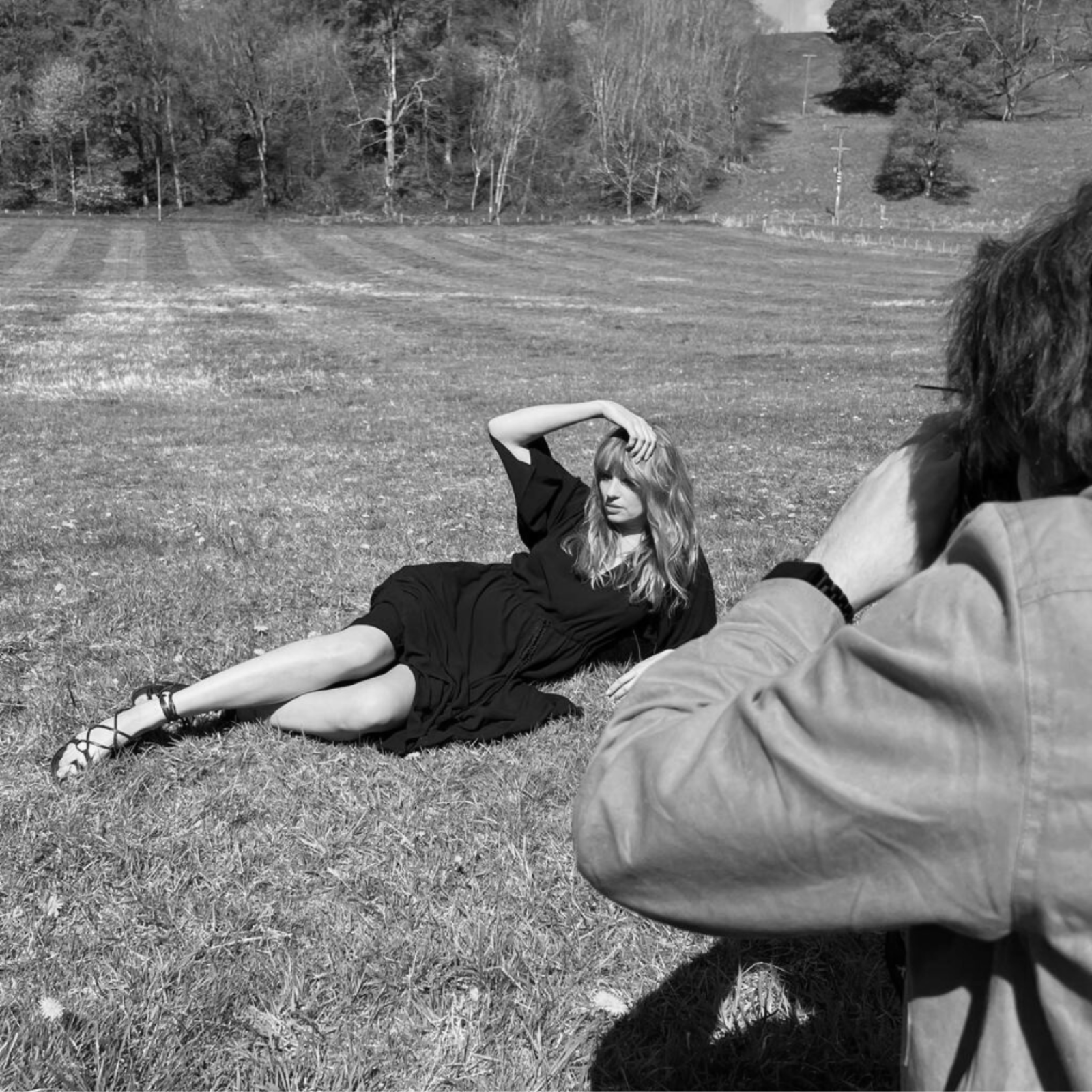 Model lying in grassy ffestival feild being shot by photographer and wearing the Blackbird Midi Dress
